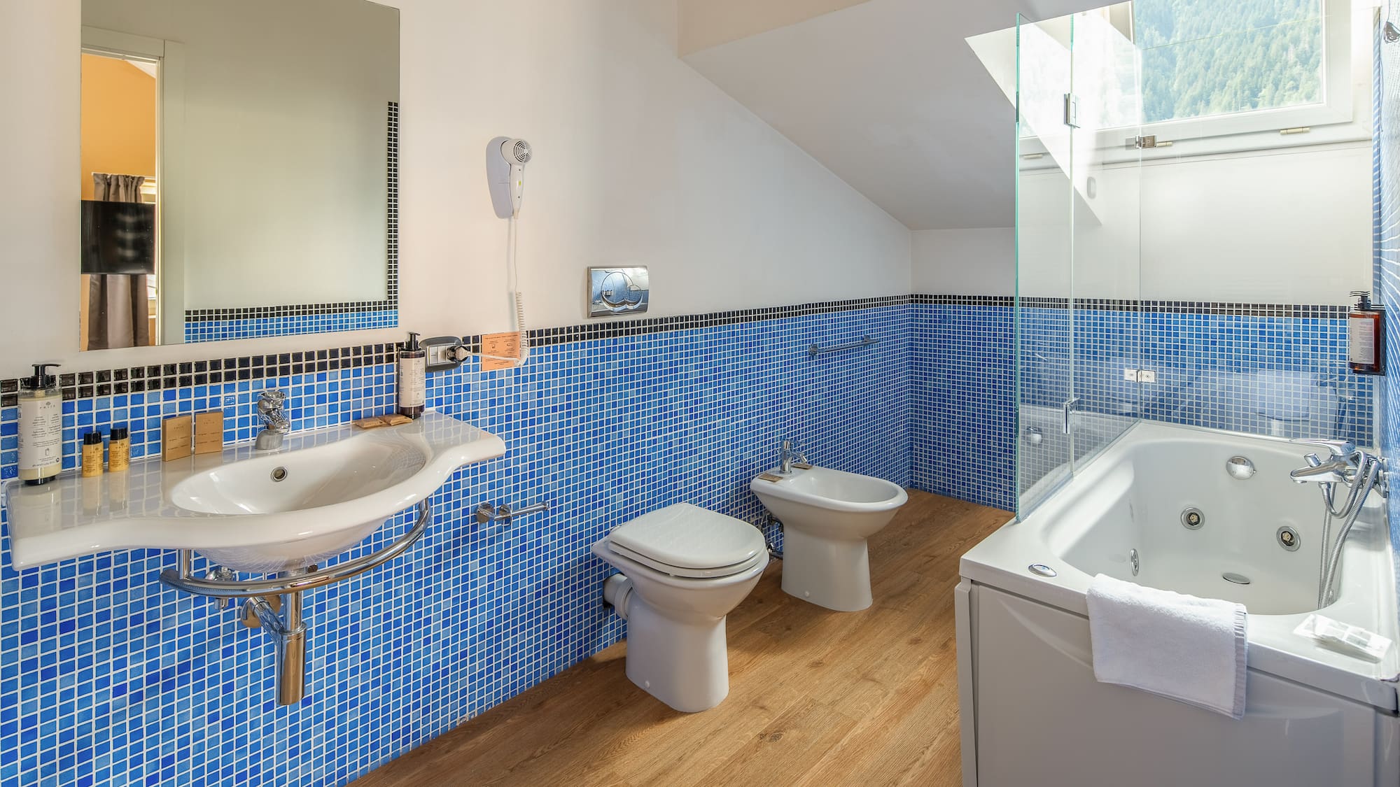 Modern blue tiled bathroom with jacuzzi tub, sink, toilet, and bidet.