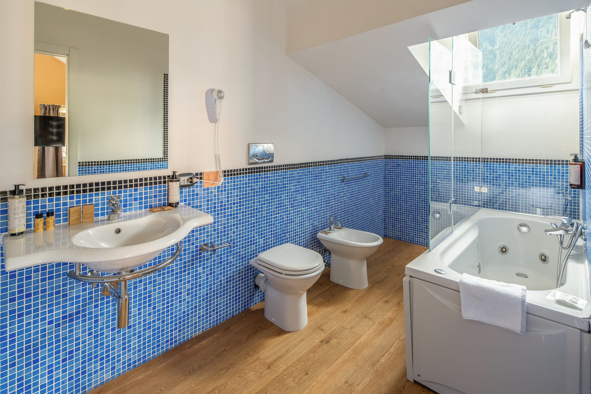 Modern blue tiled bathroom with jacuzzi tub, sink, toilet, and bidet.