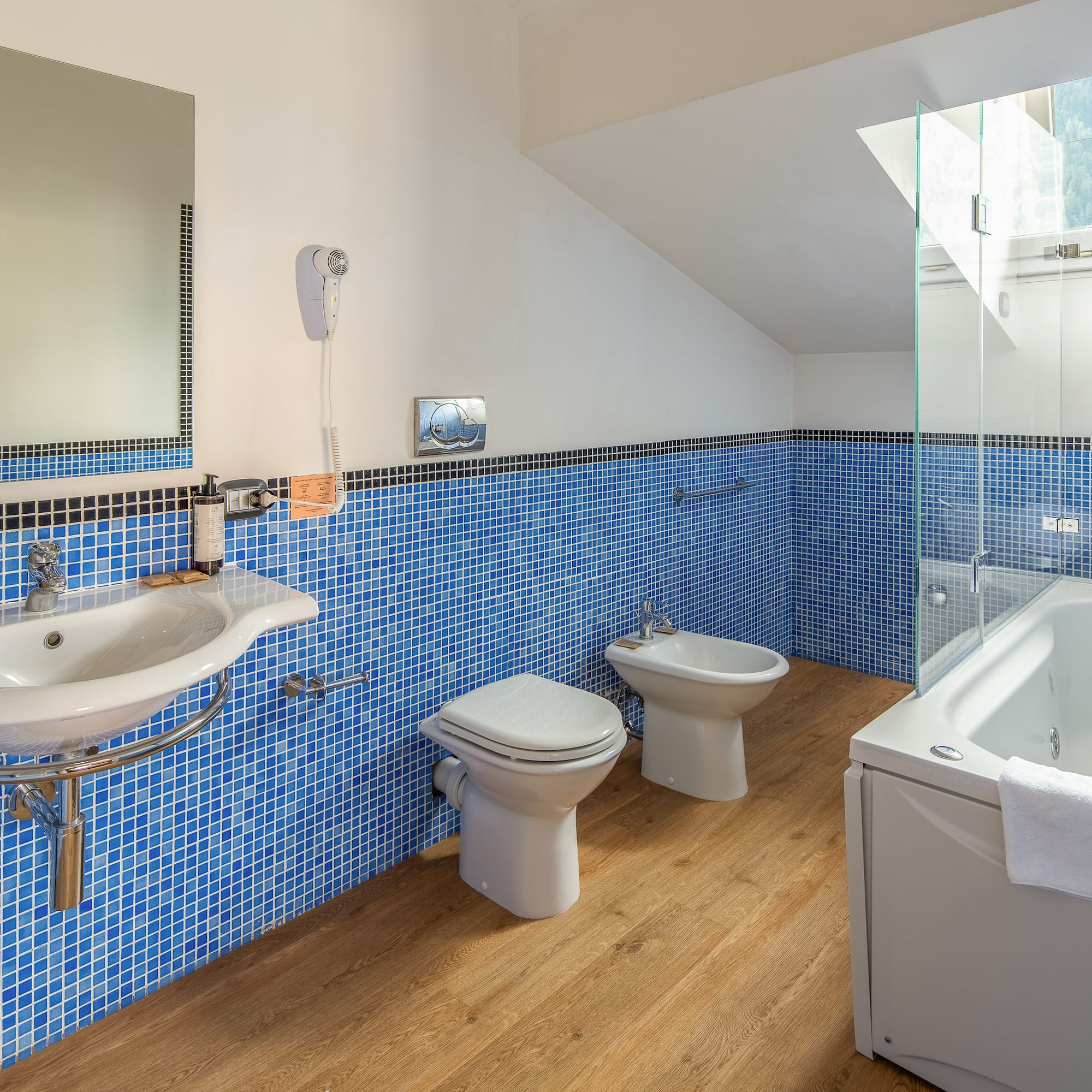 Modern blue tiled bathroom with jacuzzi tub, sink, toilet, and bidet.