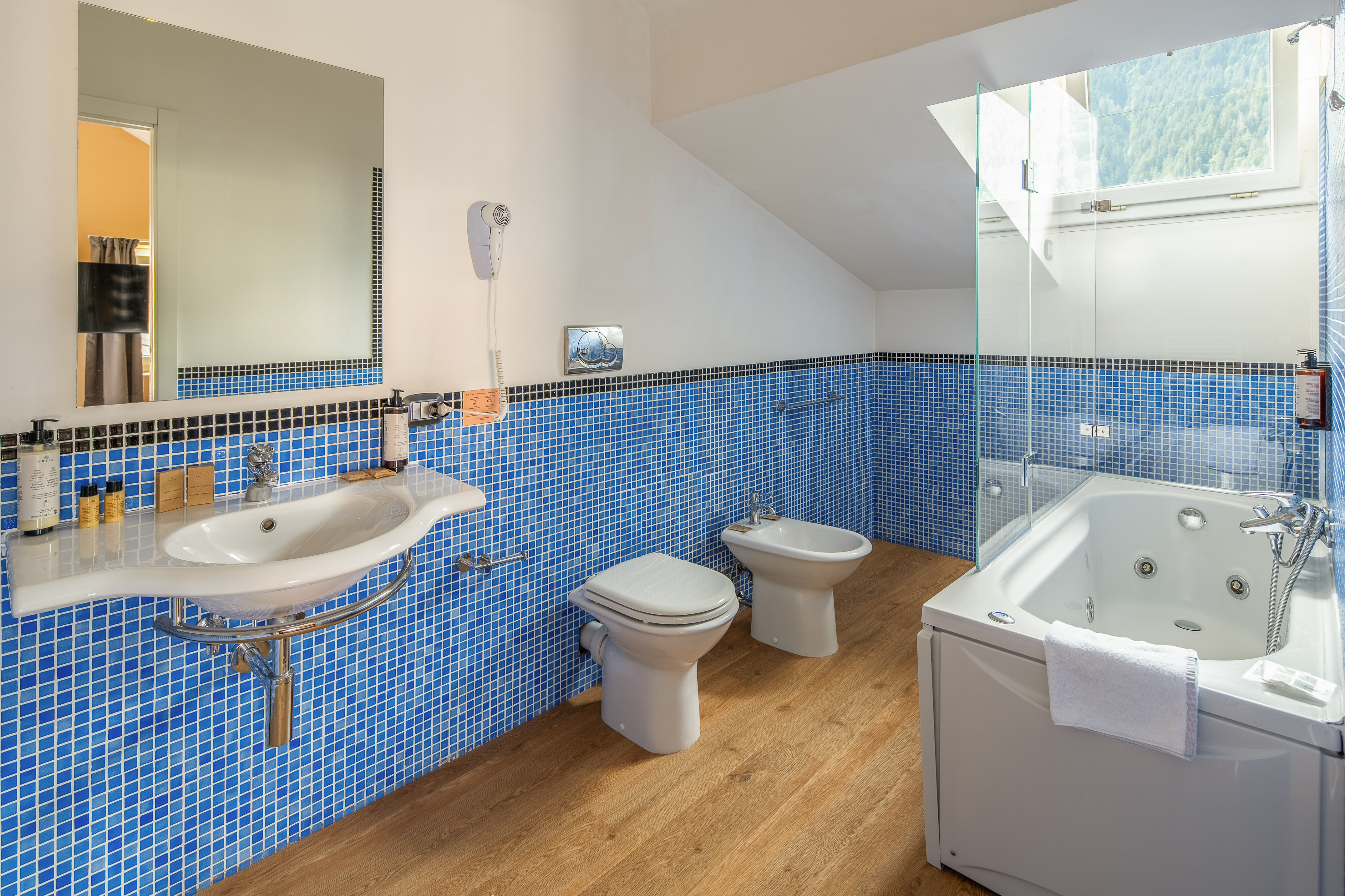 Modern blue tiled bathroom with jacuzzi tub, sink, toilet, and bidet.