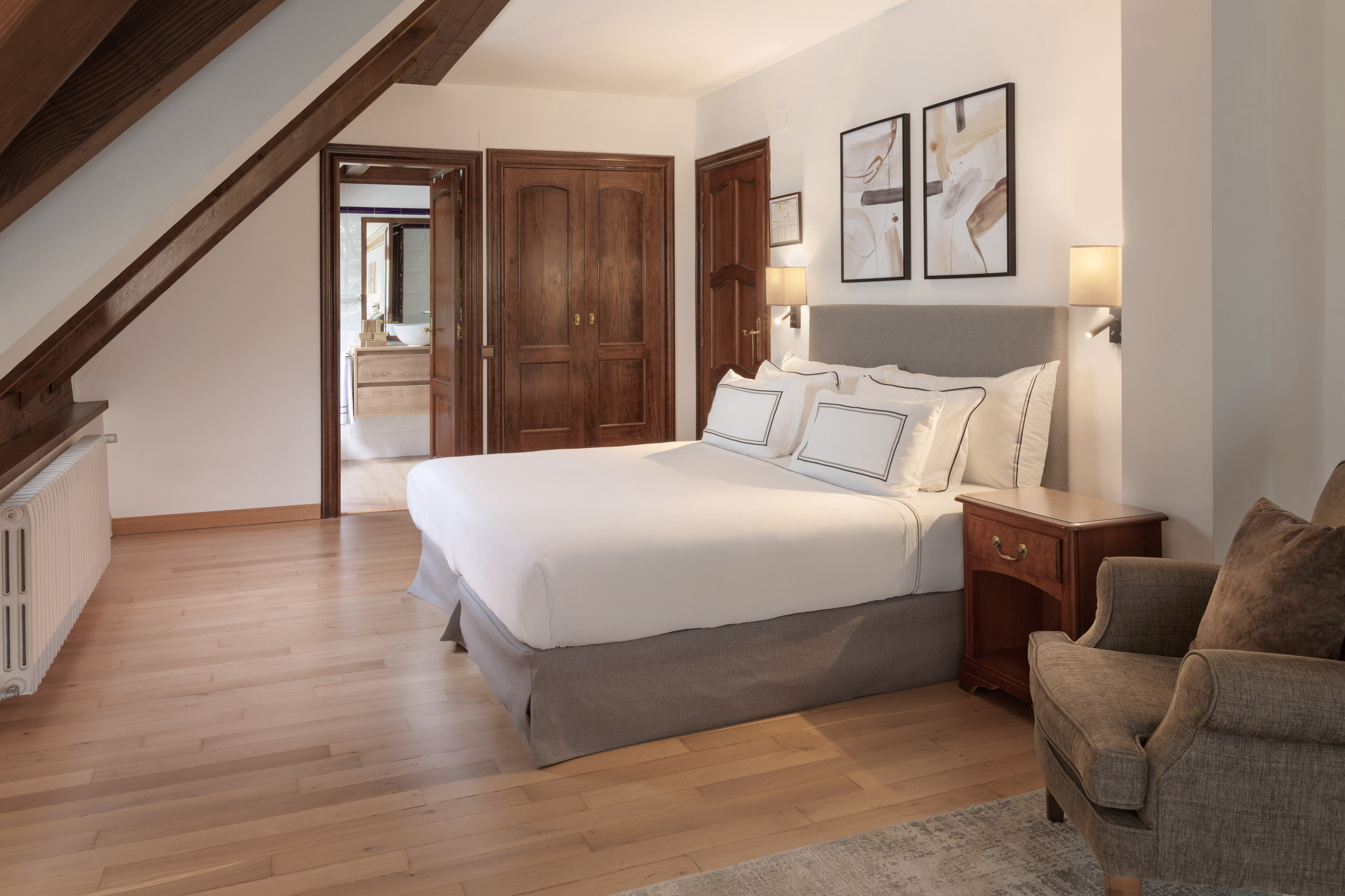 Hotel bedroom with king bed, wooden beams, hardwood floor, and elegant decor.