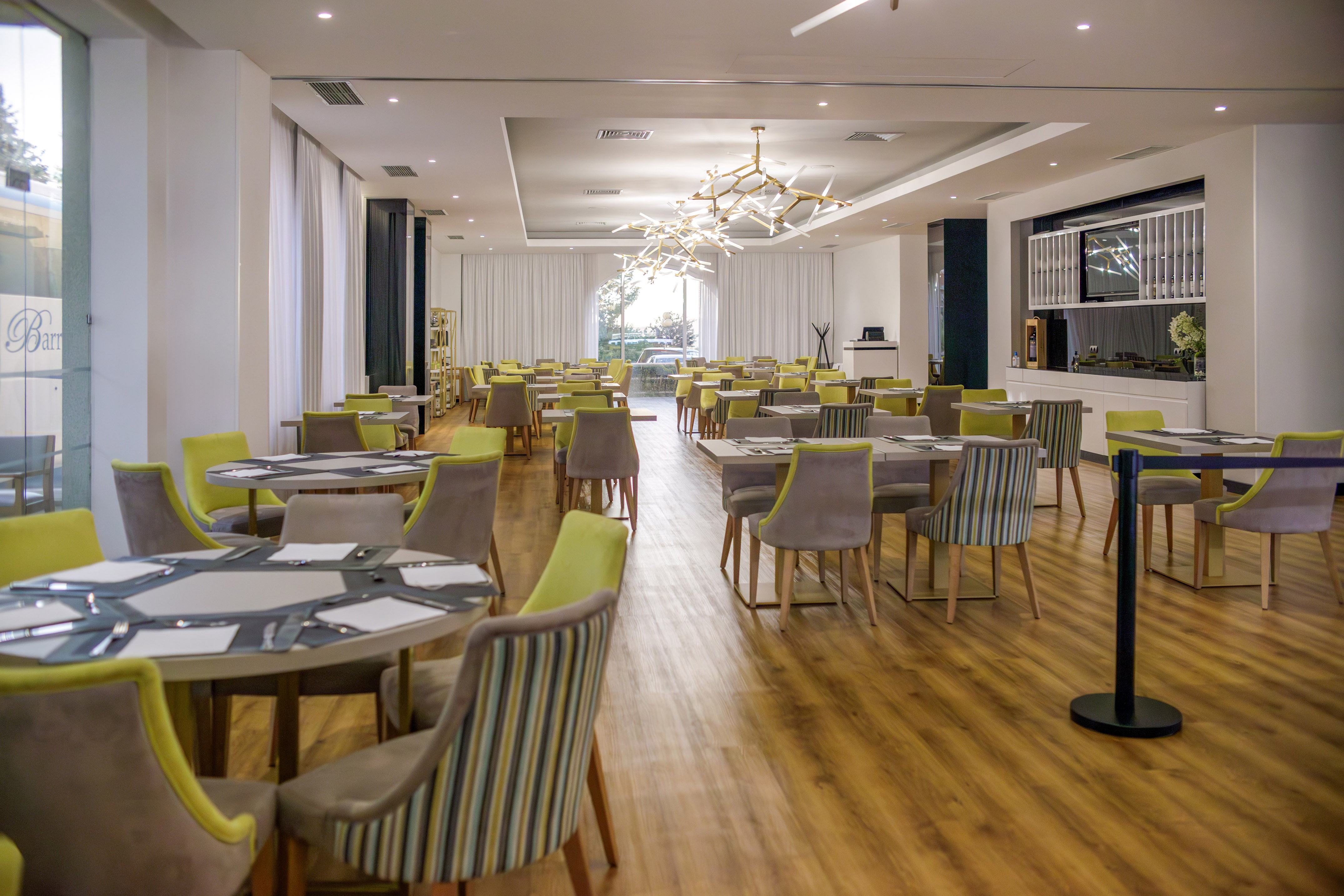 Modern hotel restaurant dining room with green chairs and stylish chandelier.