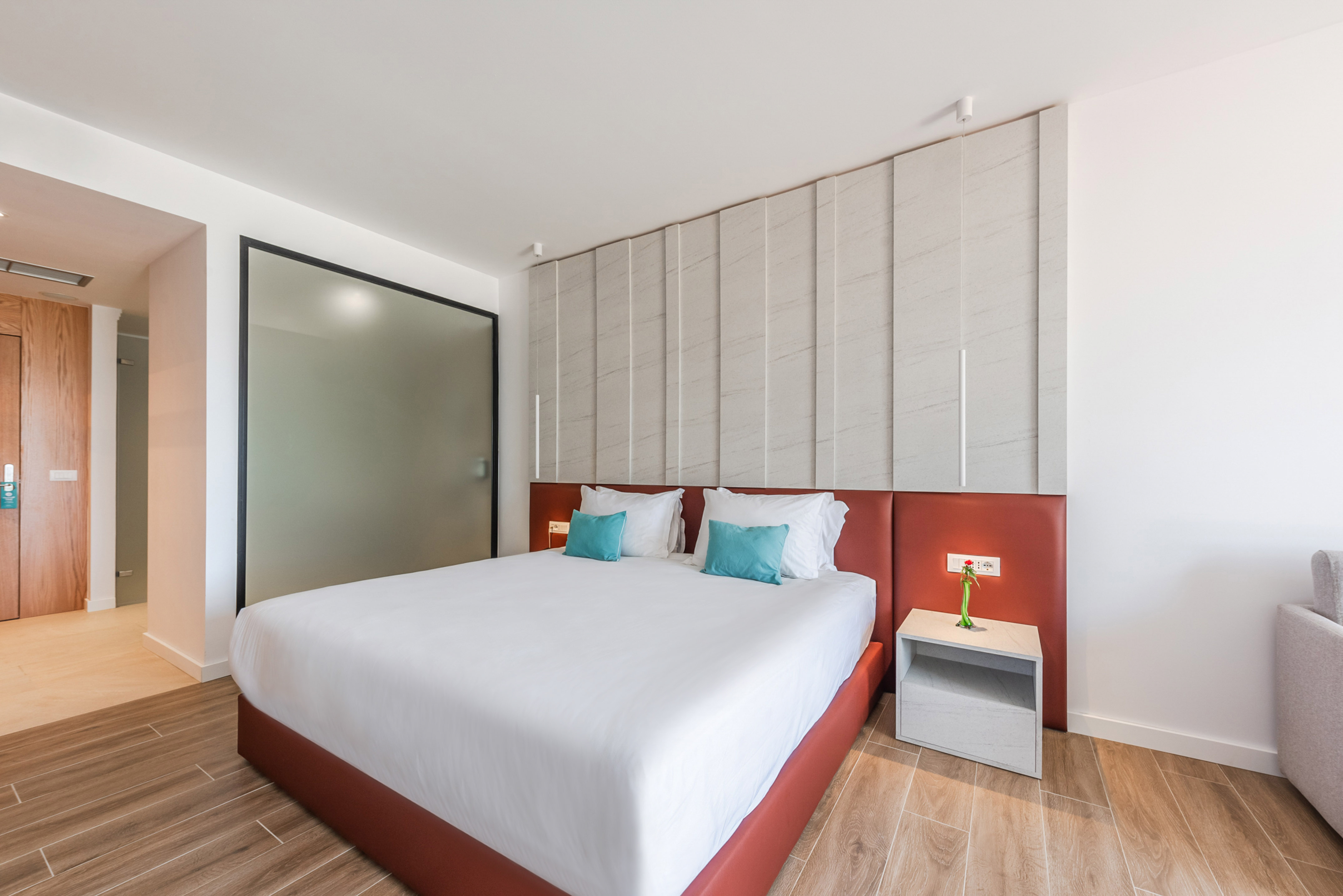 Modern hotel bedroom with large bed, red headboard, and wood floors.