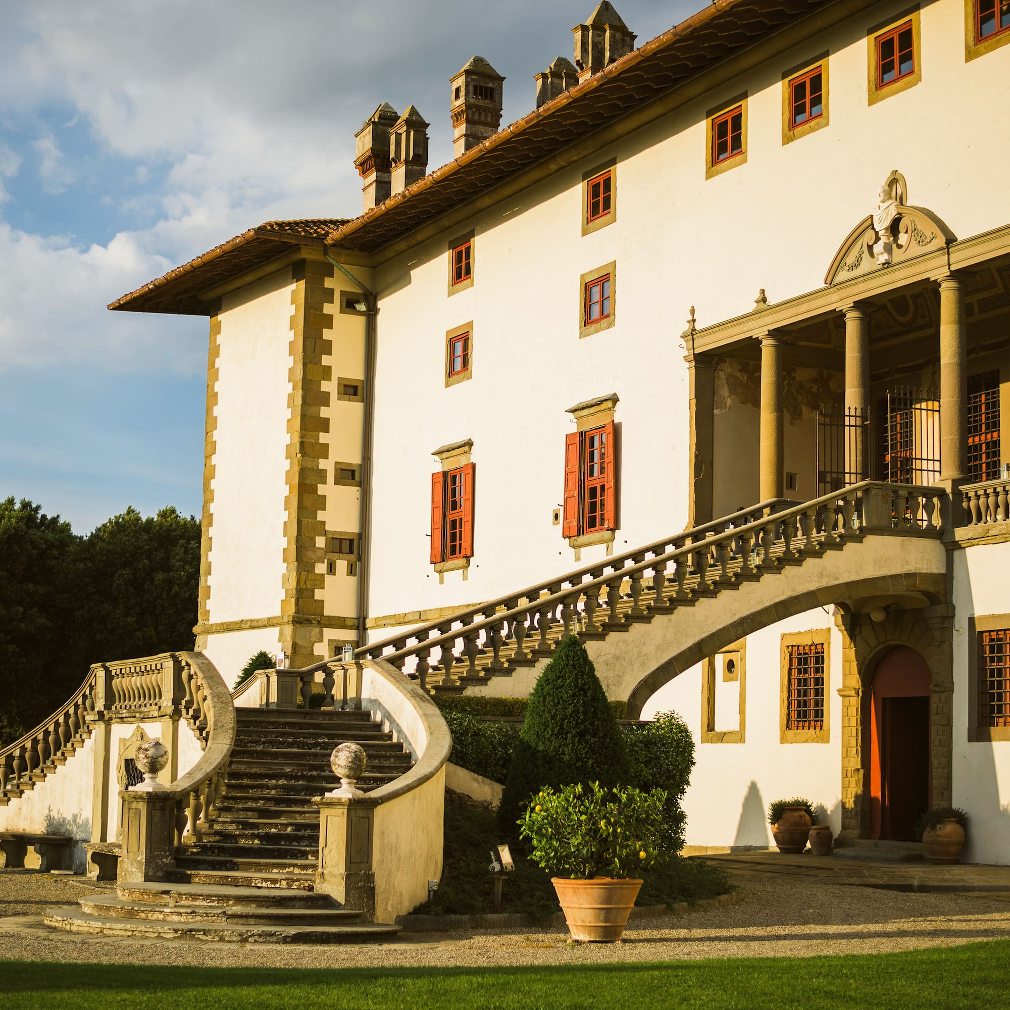 Historic Italian villa with grand stone staircase, portico, and red shutters.