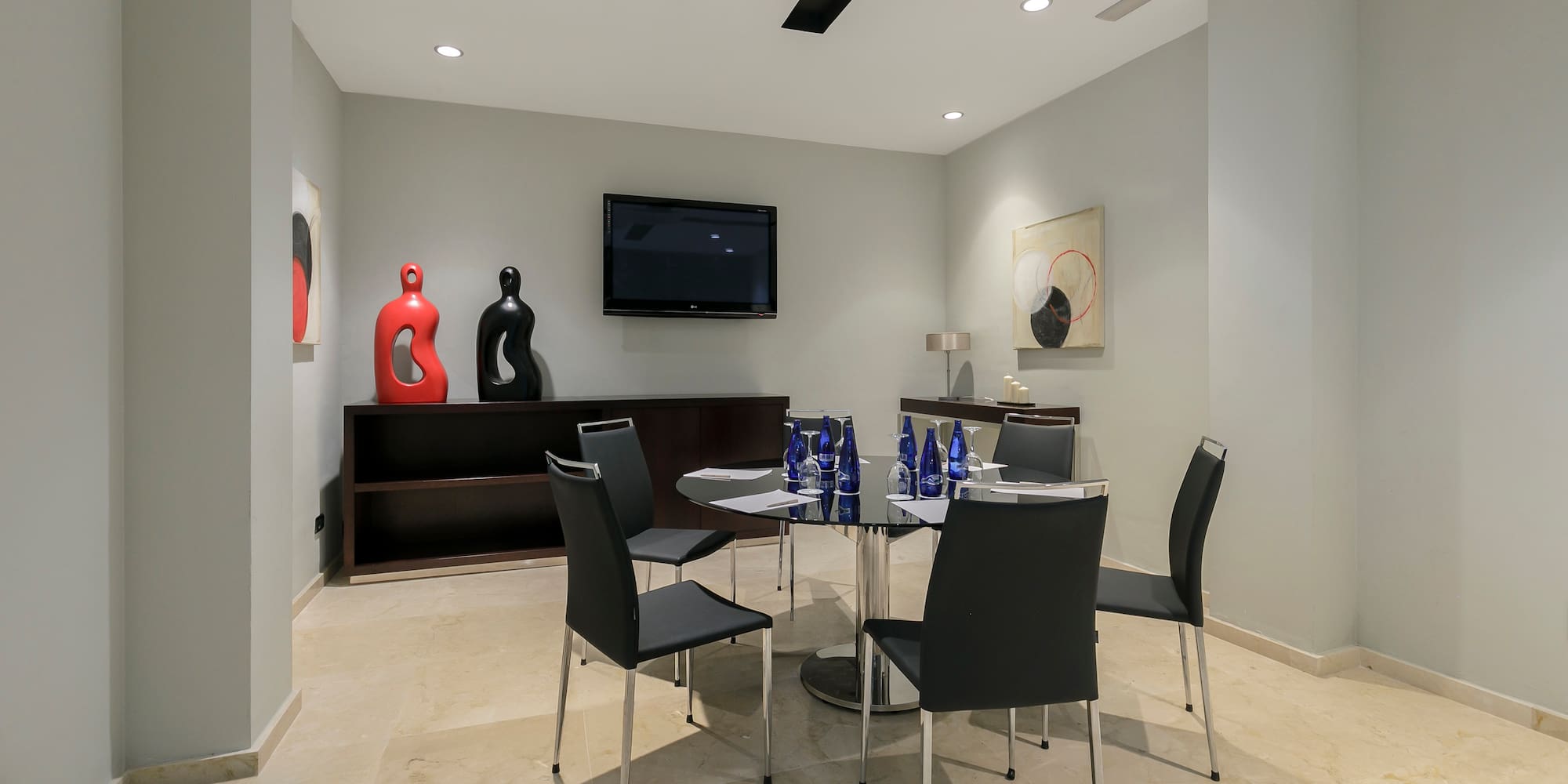 Contemporary meeting room with round table, black chairs, wall TV, modern decor.