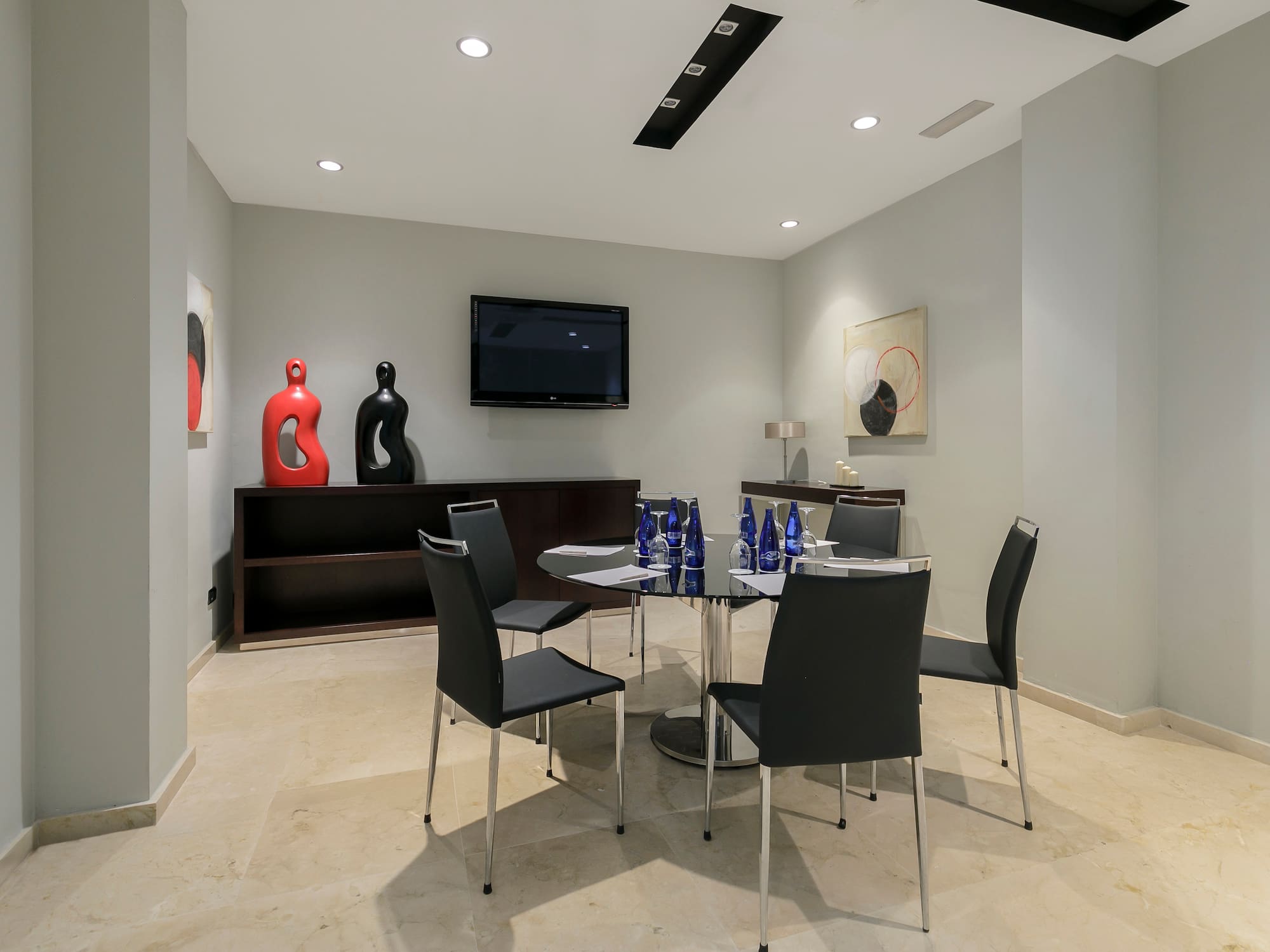 Modern meeting room with glass table, black chairs, TV, and contemporary decor.