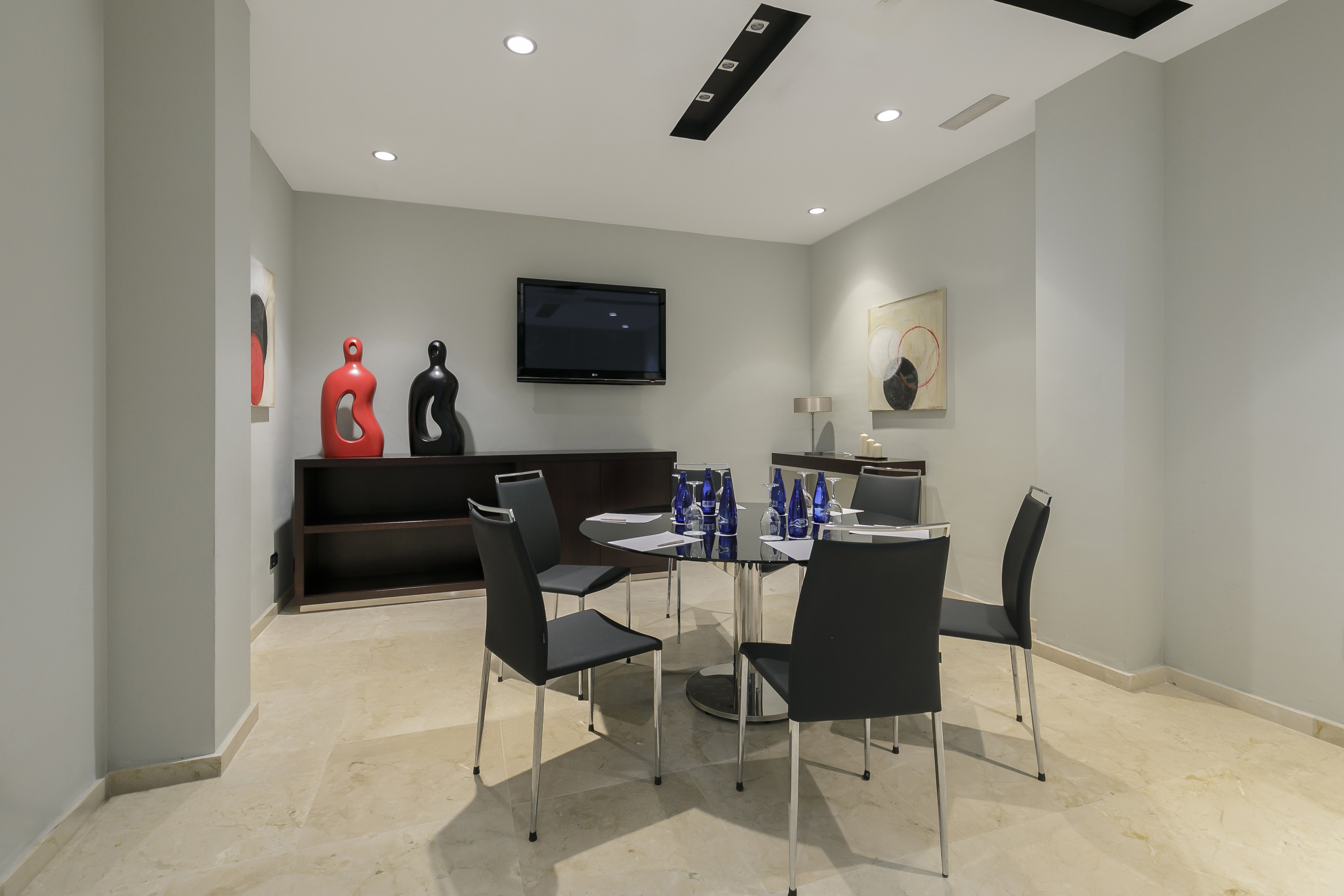 Contemporary meeting room with round table, black chairs, wall TV, modern decor.
