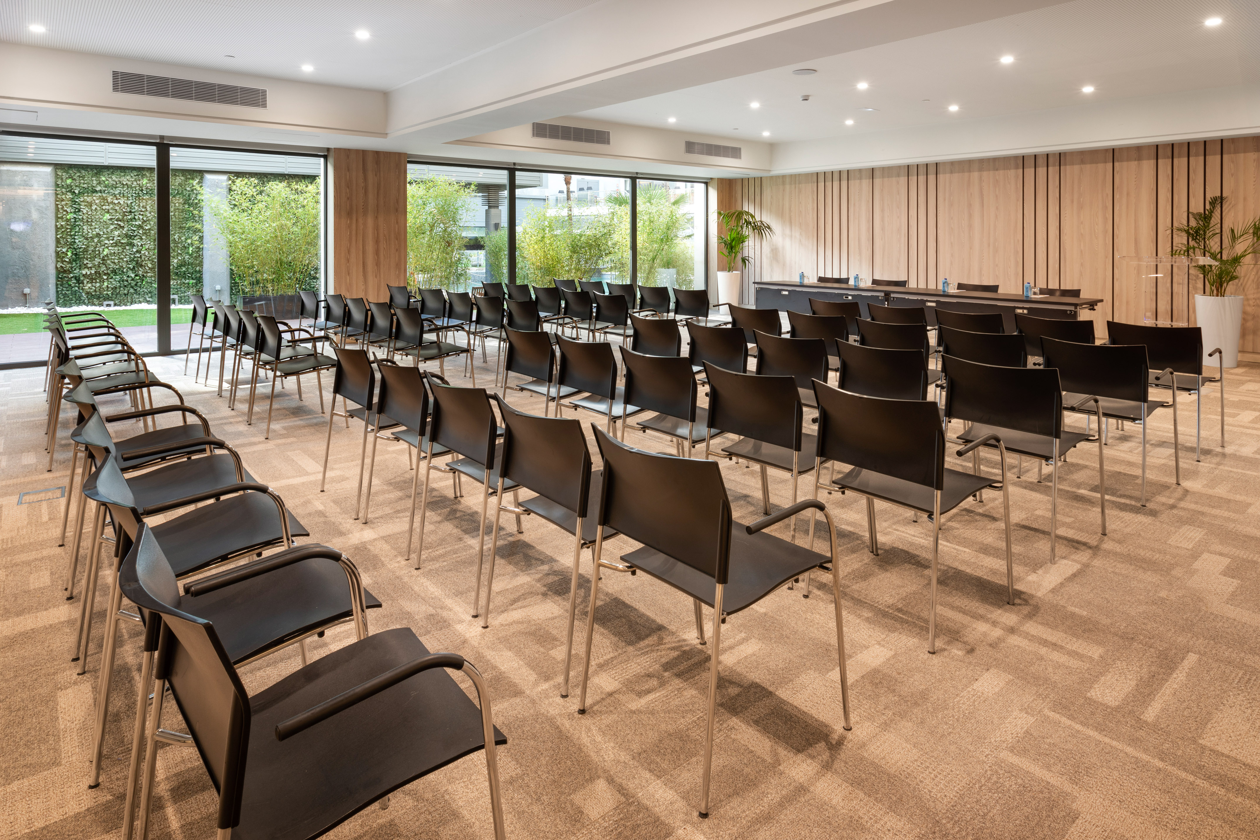 Modern conference room with black chairs, wooden walls, natural light and green views.