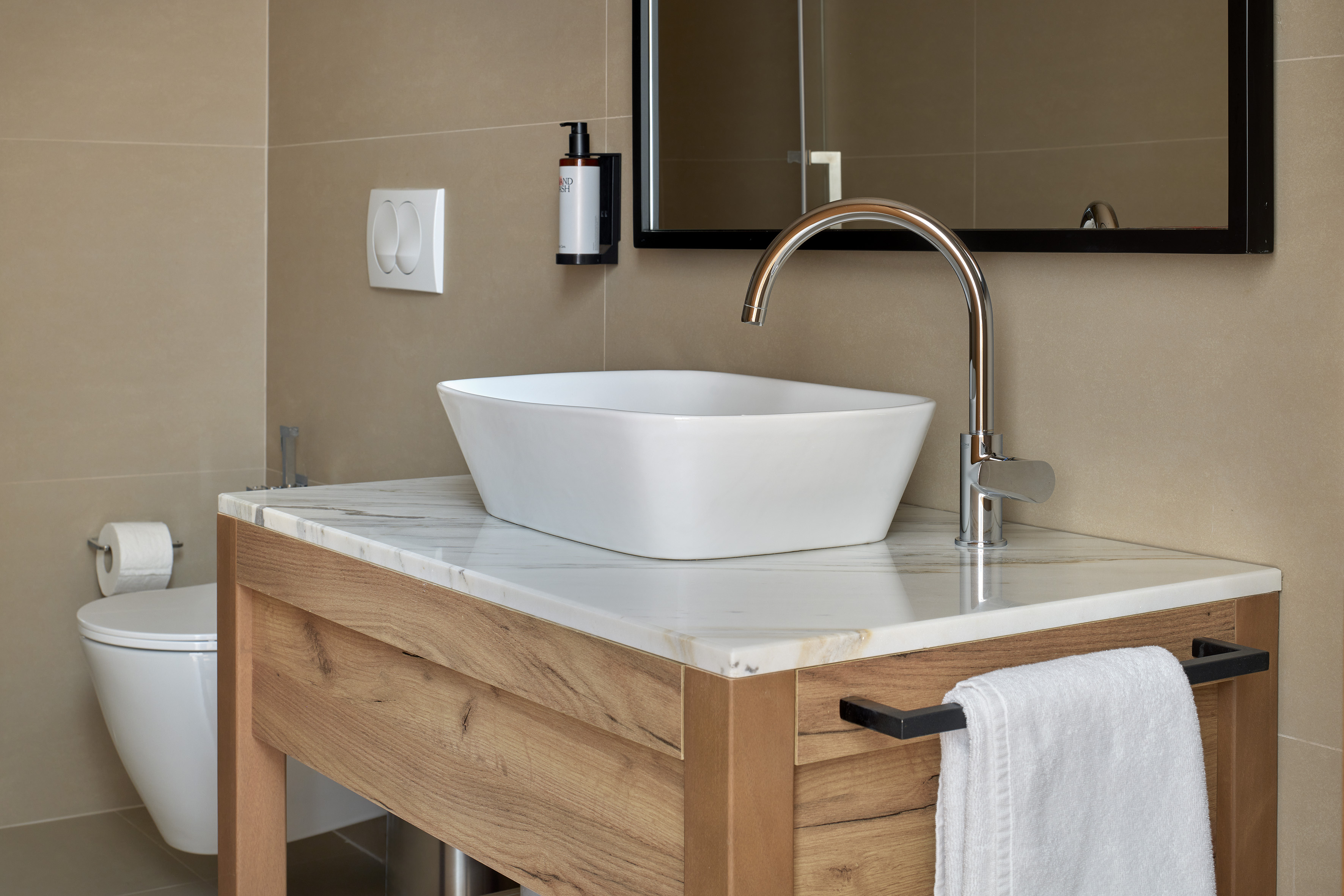 Modern bathroom vanity: white vessel sink, marble top, wood base, chrome faucet.