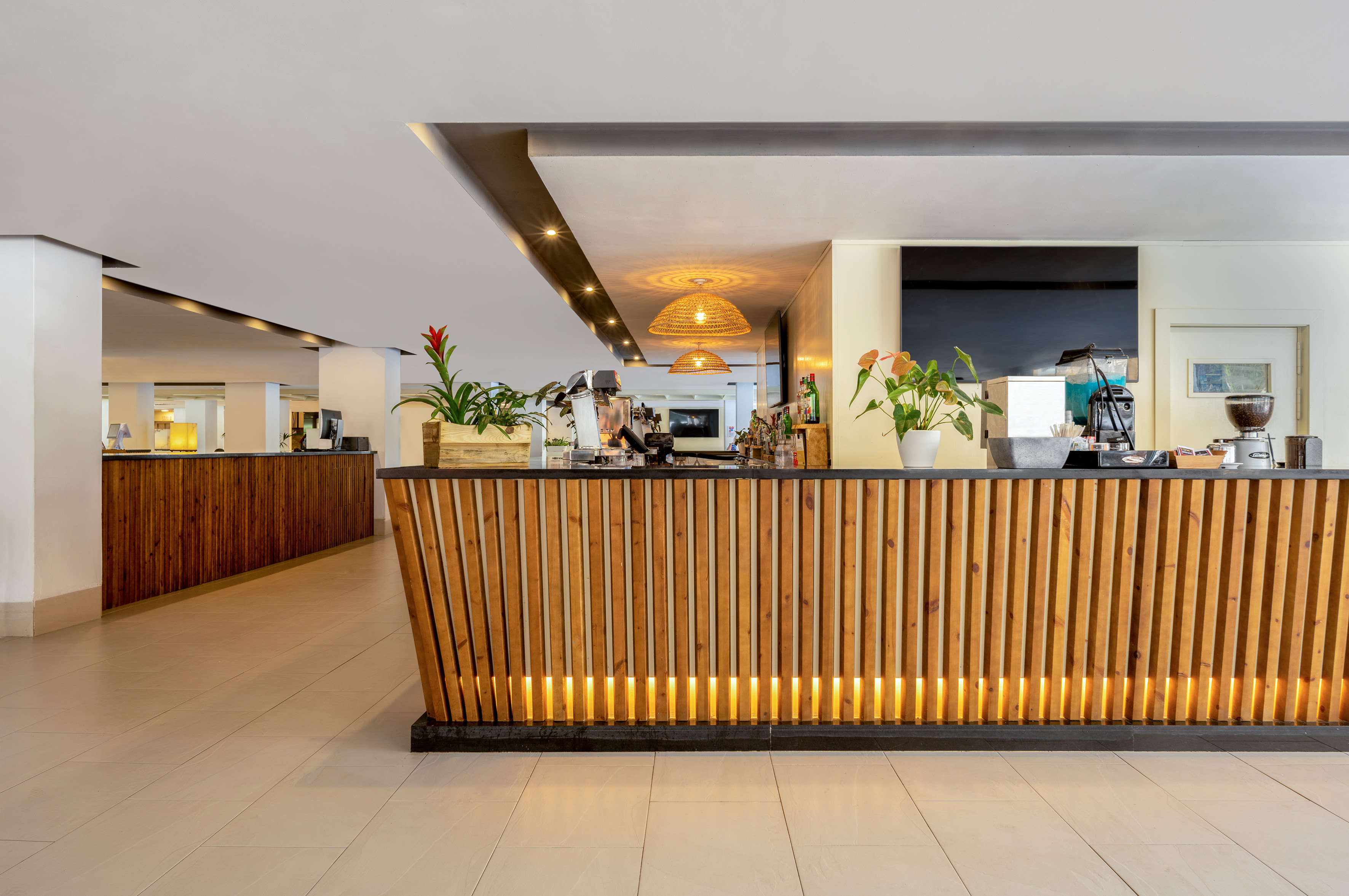 Modern wooden slatted hotel bar counter with coffee station and warm lighting.