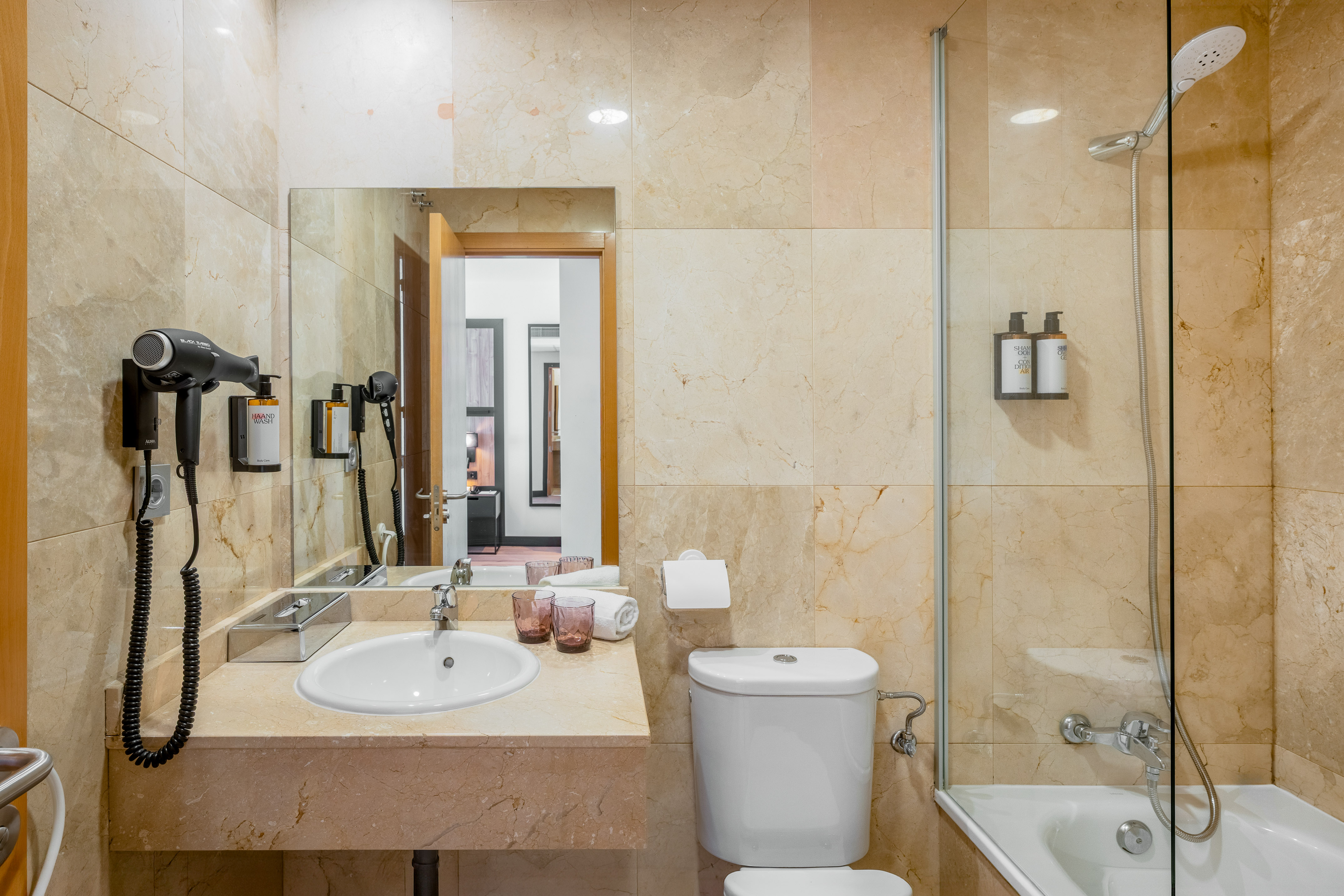 Clean hotel bathroom with marble vanity, sink, toilet, and shower.