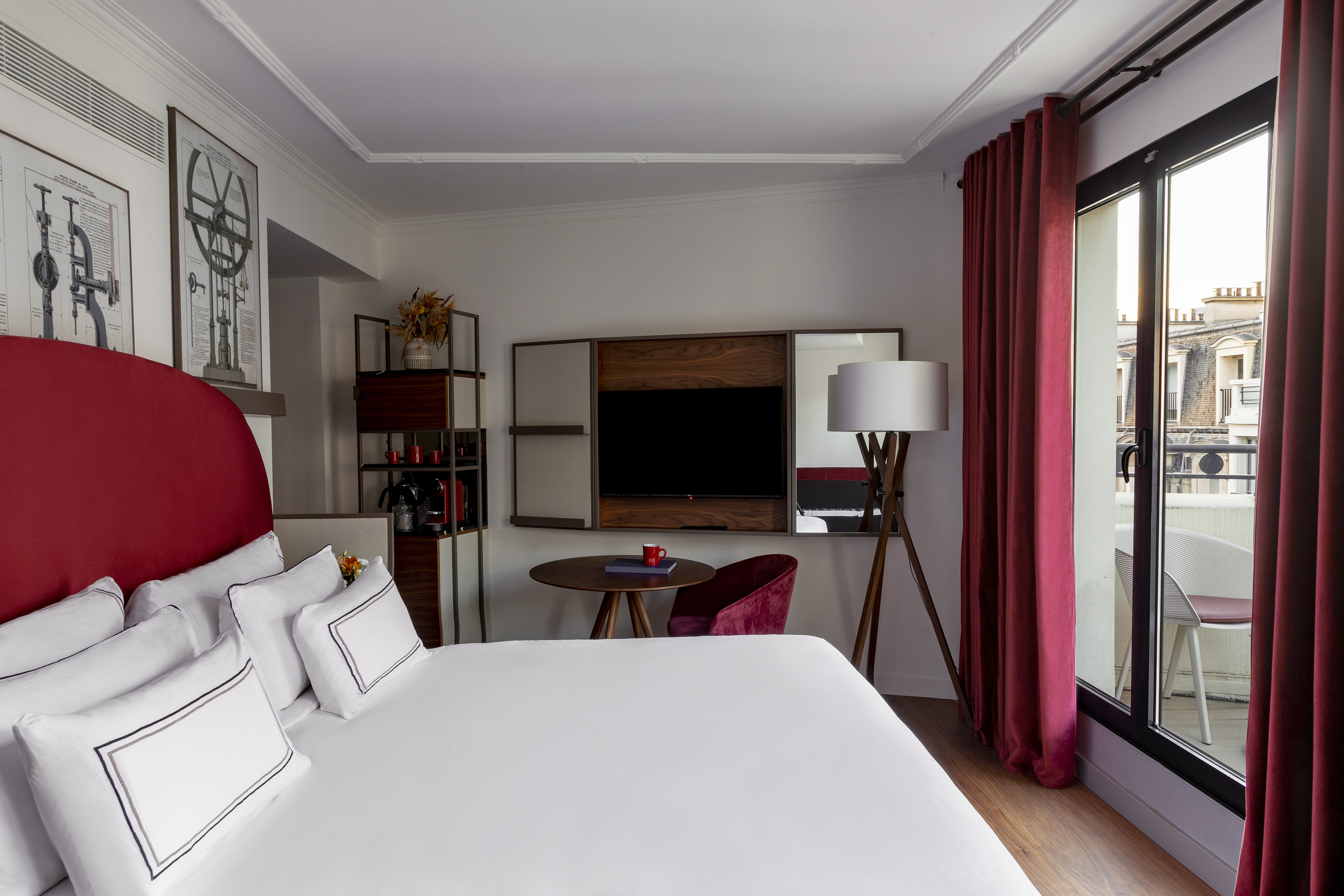 Modern hotel room with red bed, balcony, city view, and white linens.