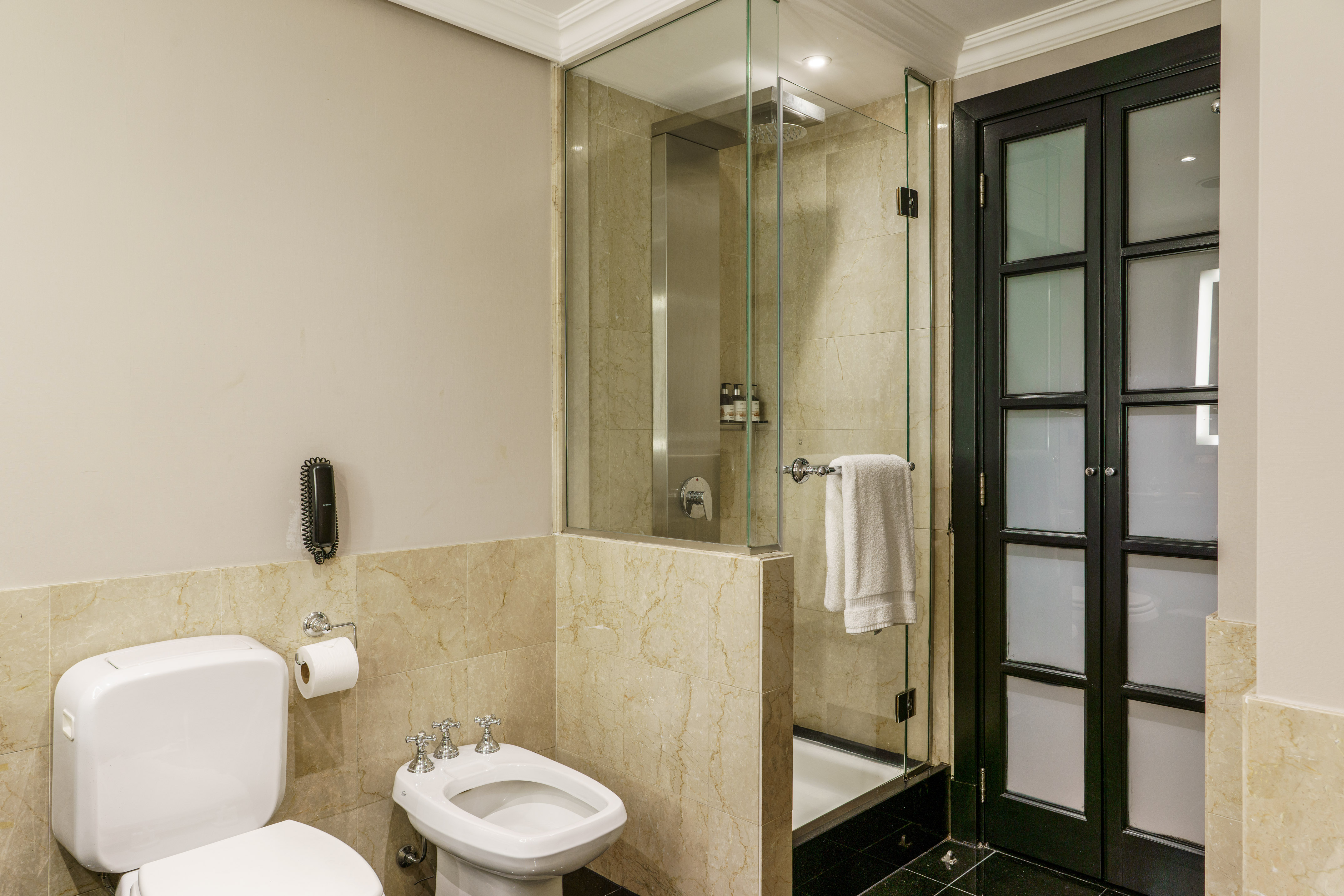 Modern hotel bathroom with toilet, bidet, glass shower, and marble walls.
