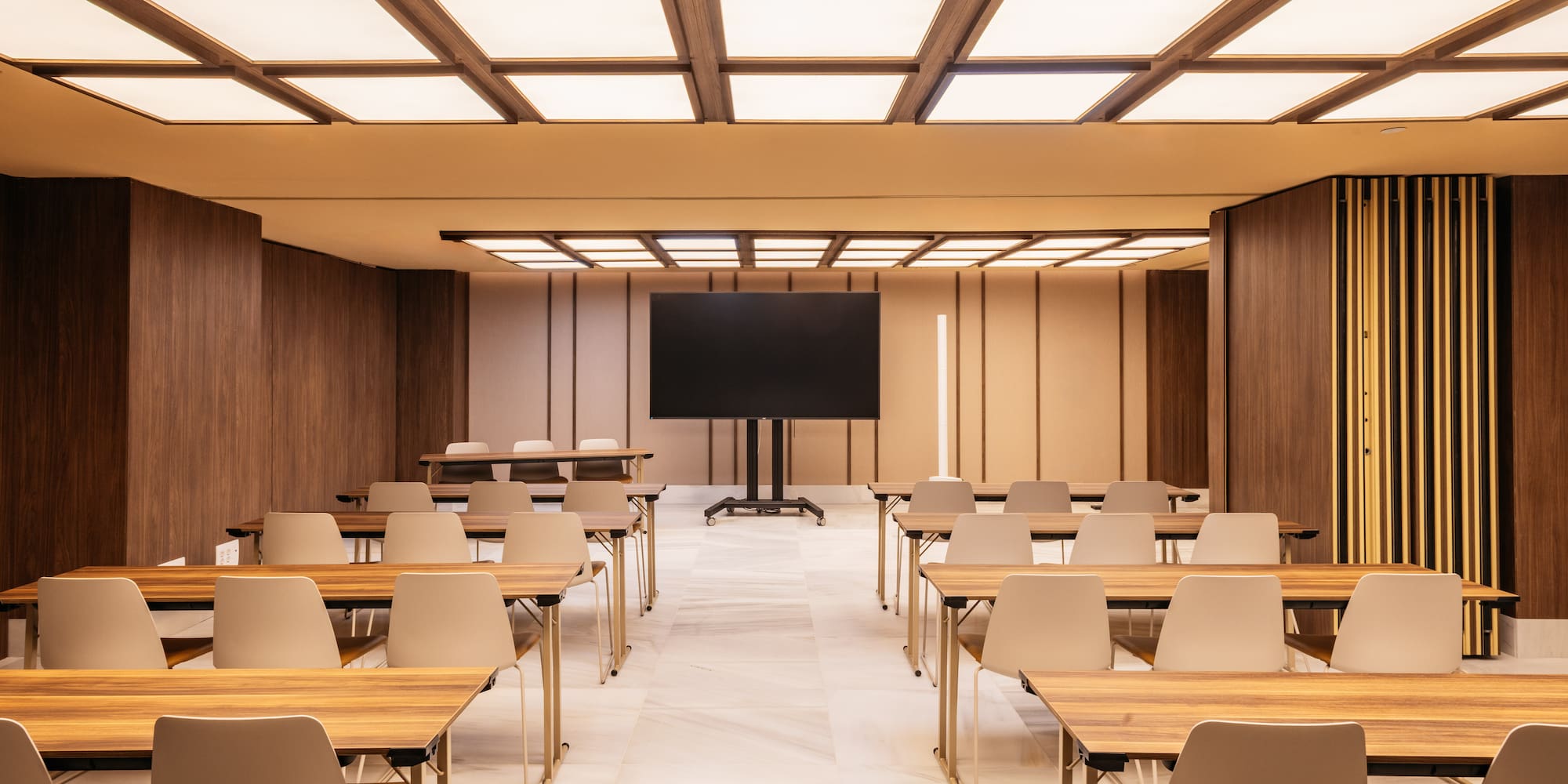 Modern conference room with tables, chairs, large screen, bright ceiling.