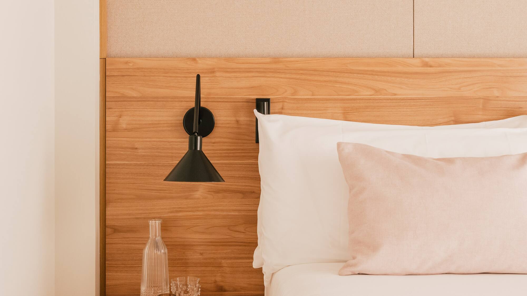 Modern bedroom: wood headboard, white bed, pink pillow, and bedside table.