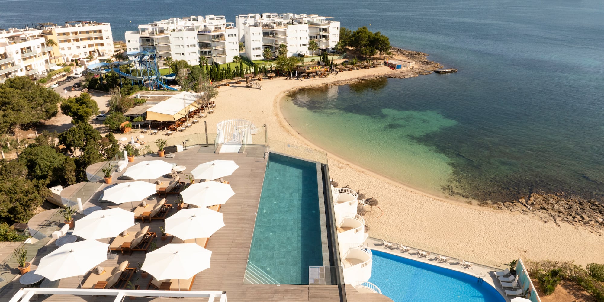 a pool and beach with buildings and water in the background