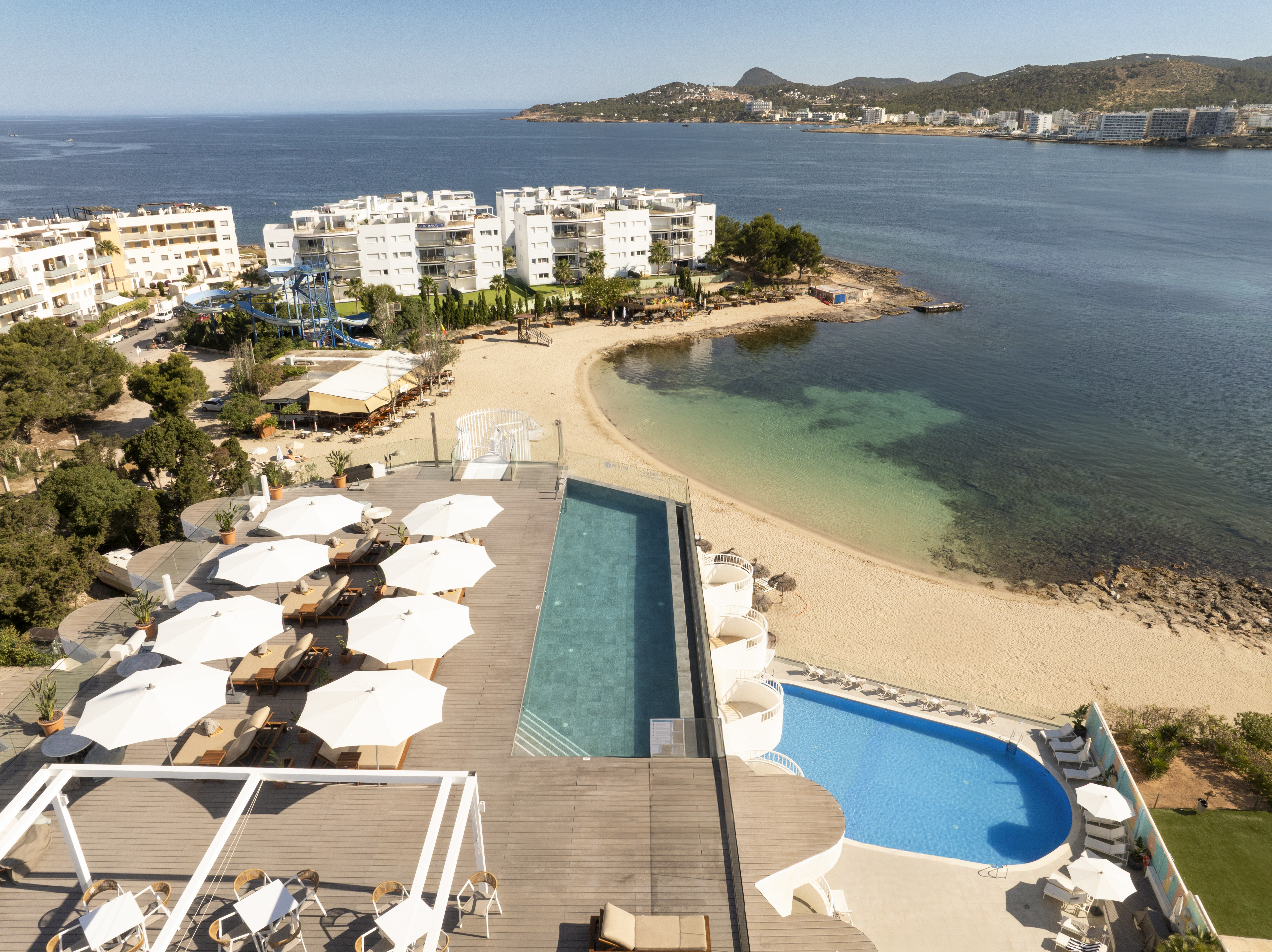Luxury hotel infinity pool deck, sun loungers, sandy beach, and ocean bay.