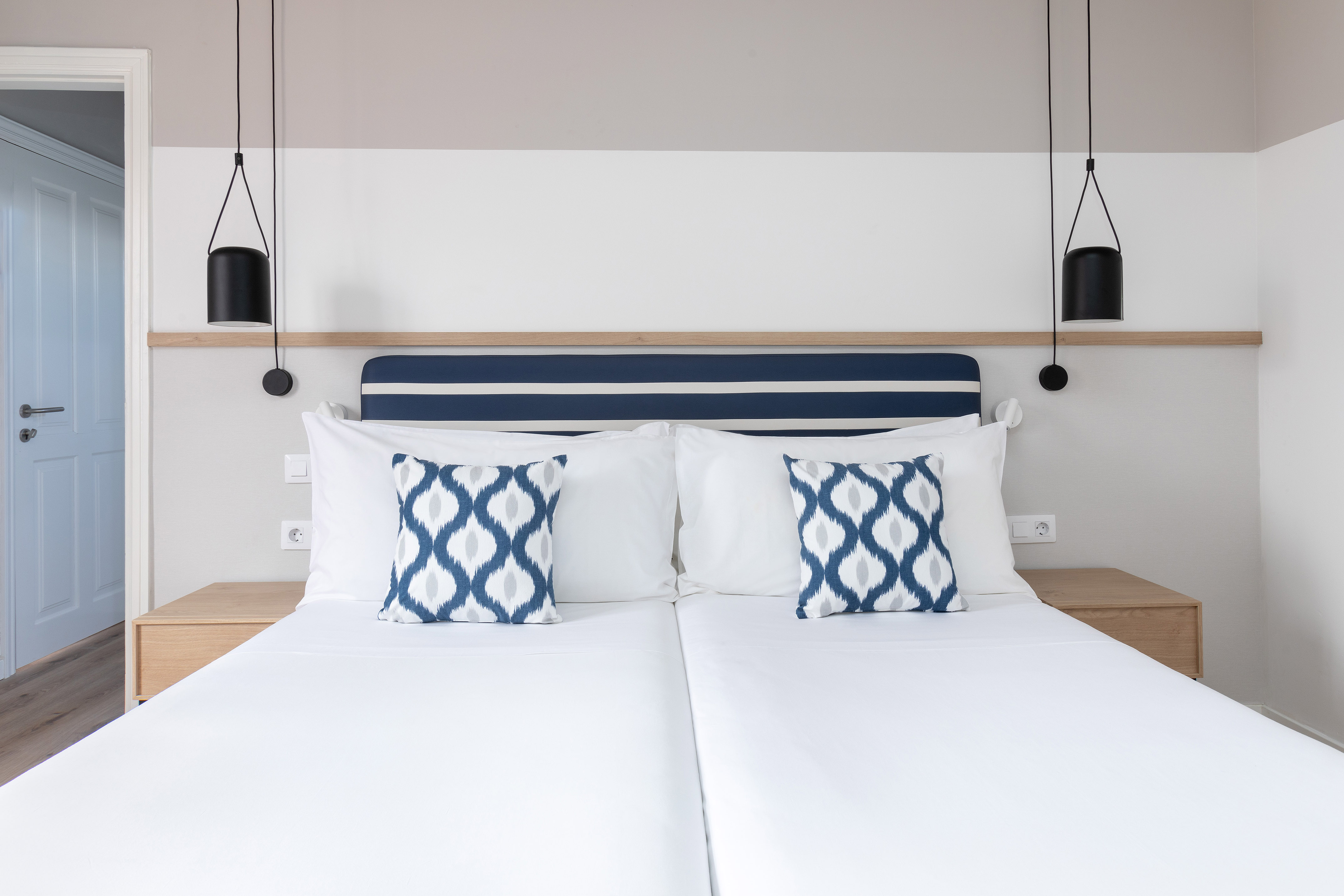 Twin bed hotel room with white linens, blue headboard, and modern pendant lights.