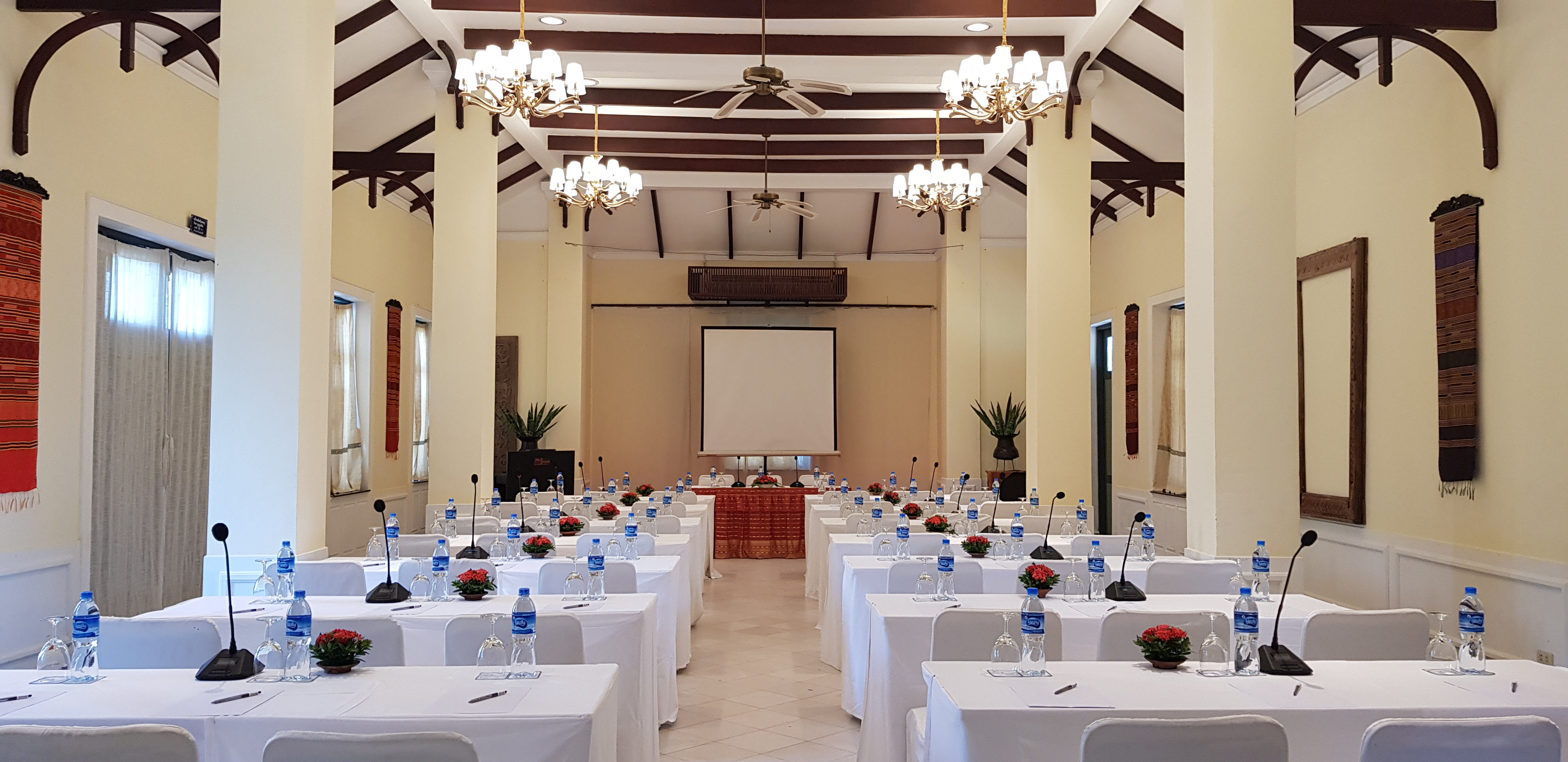 Conference room setup with white tables, microphones, and a projector screen.