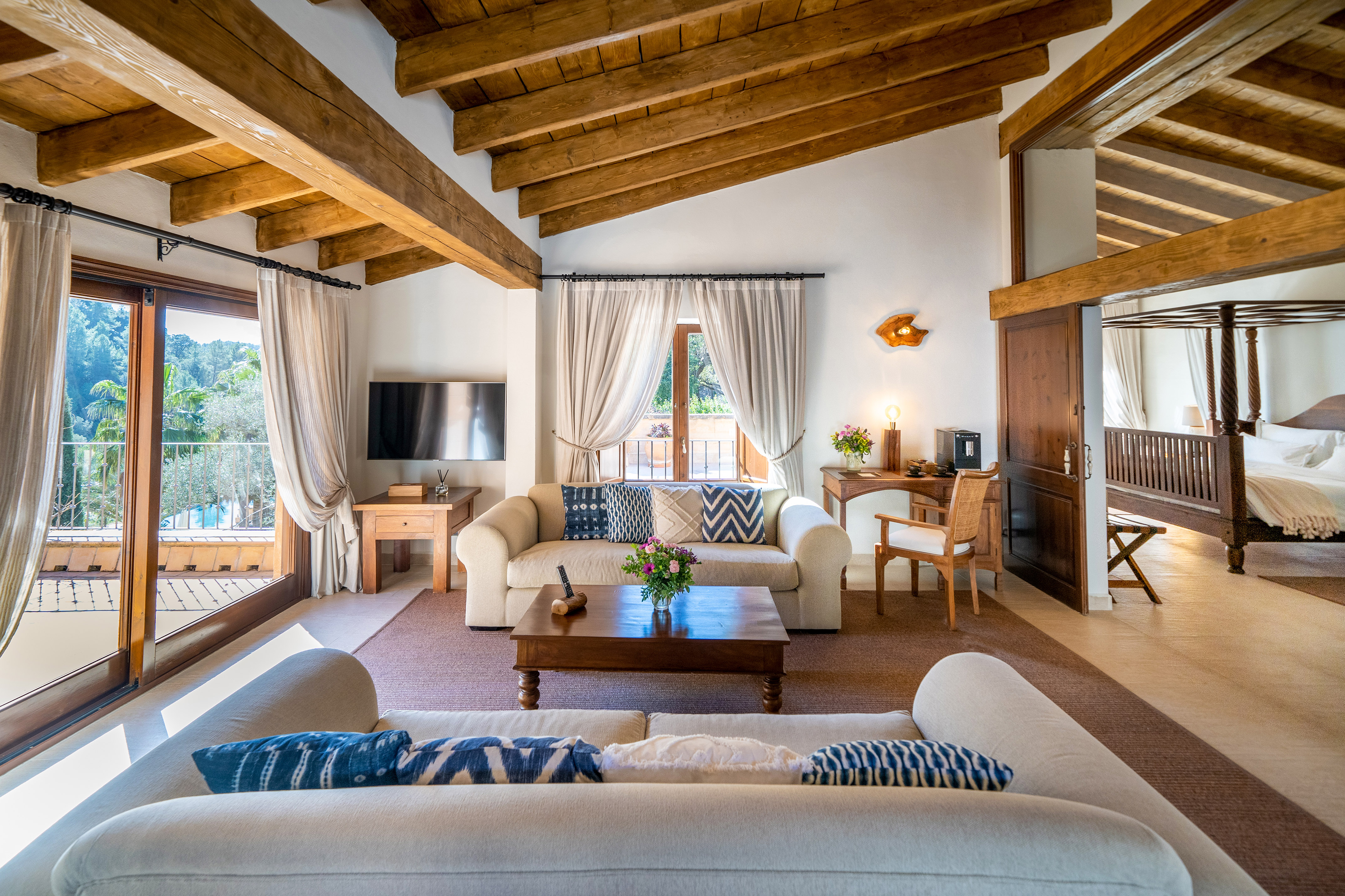 Rustic living room with exposed wooden beams, sofas, balcony, and bedroom.
