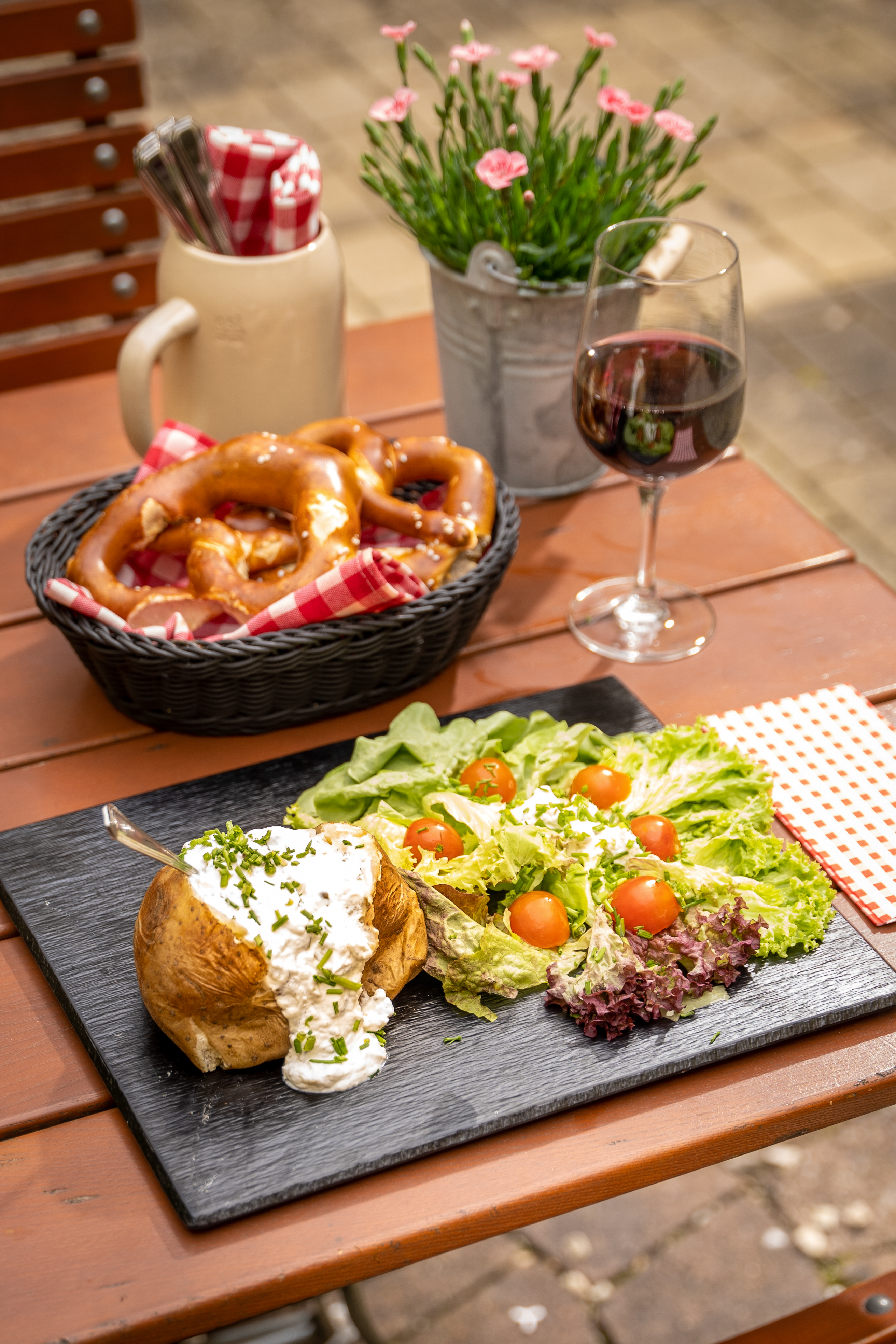 Baked potato with sour cream, fresh salad, pretzels, and red wine outdoors.