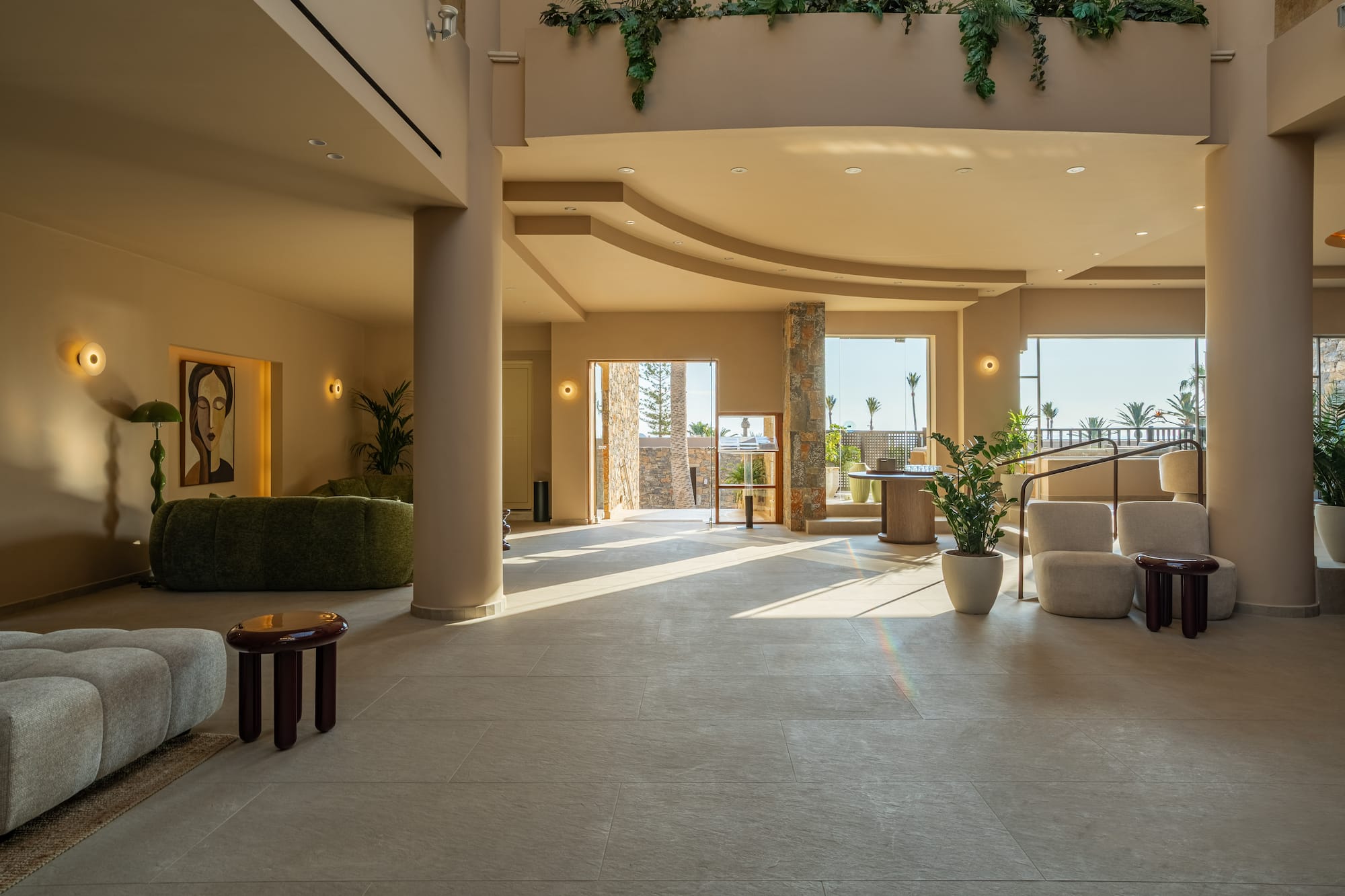 Elegant resort lobby with warm natural light, modern seating, and palm tree views.