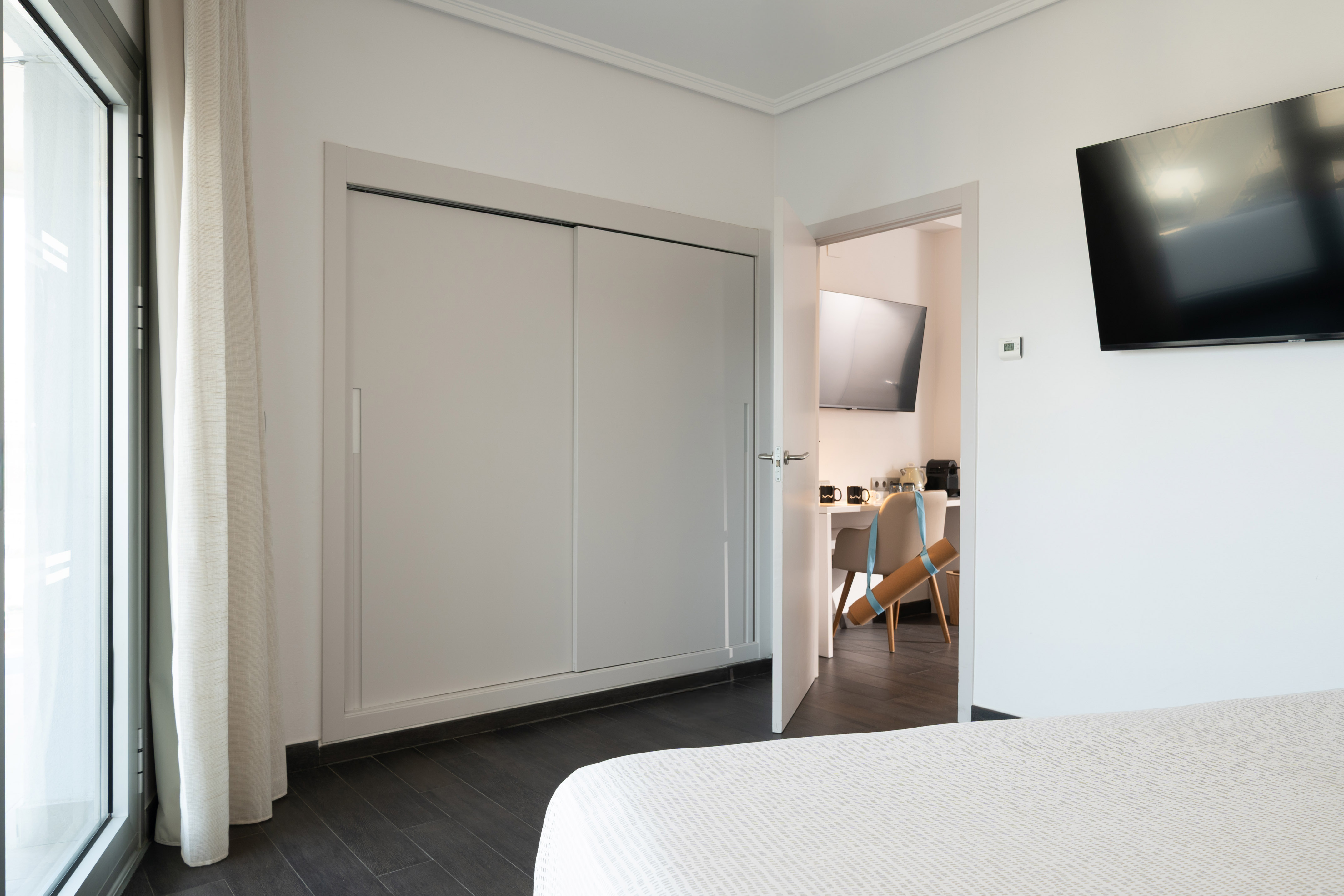 Modern bedroom interior with sliding closet, large window, and wall-mounted TV.