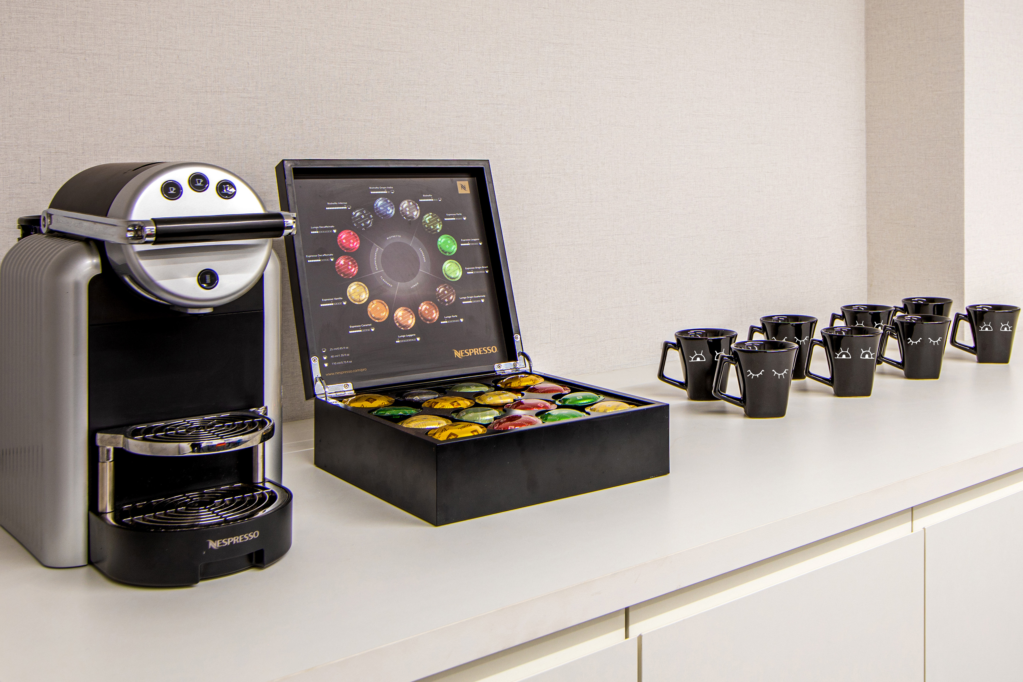 Nespresso coffee machine, colorful capsules, and black espresso cups on counter.