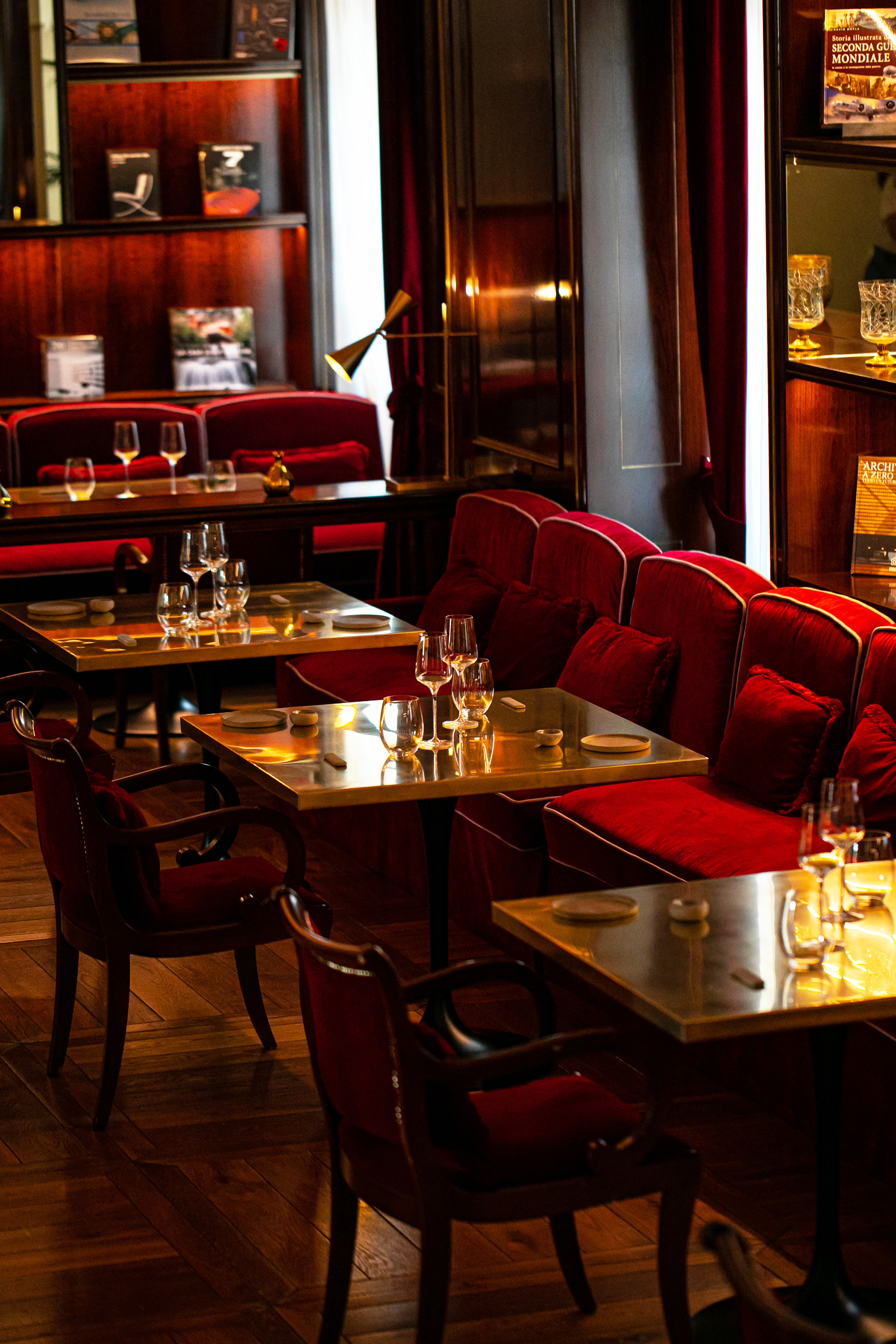 Elegant dining room with red velvet banquettes, gold tables, and warm lighting.