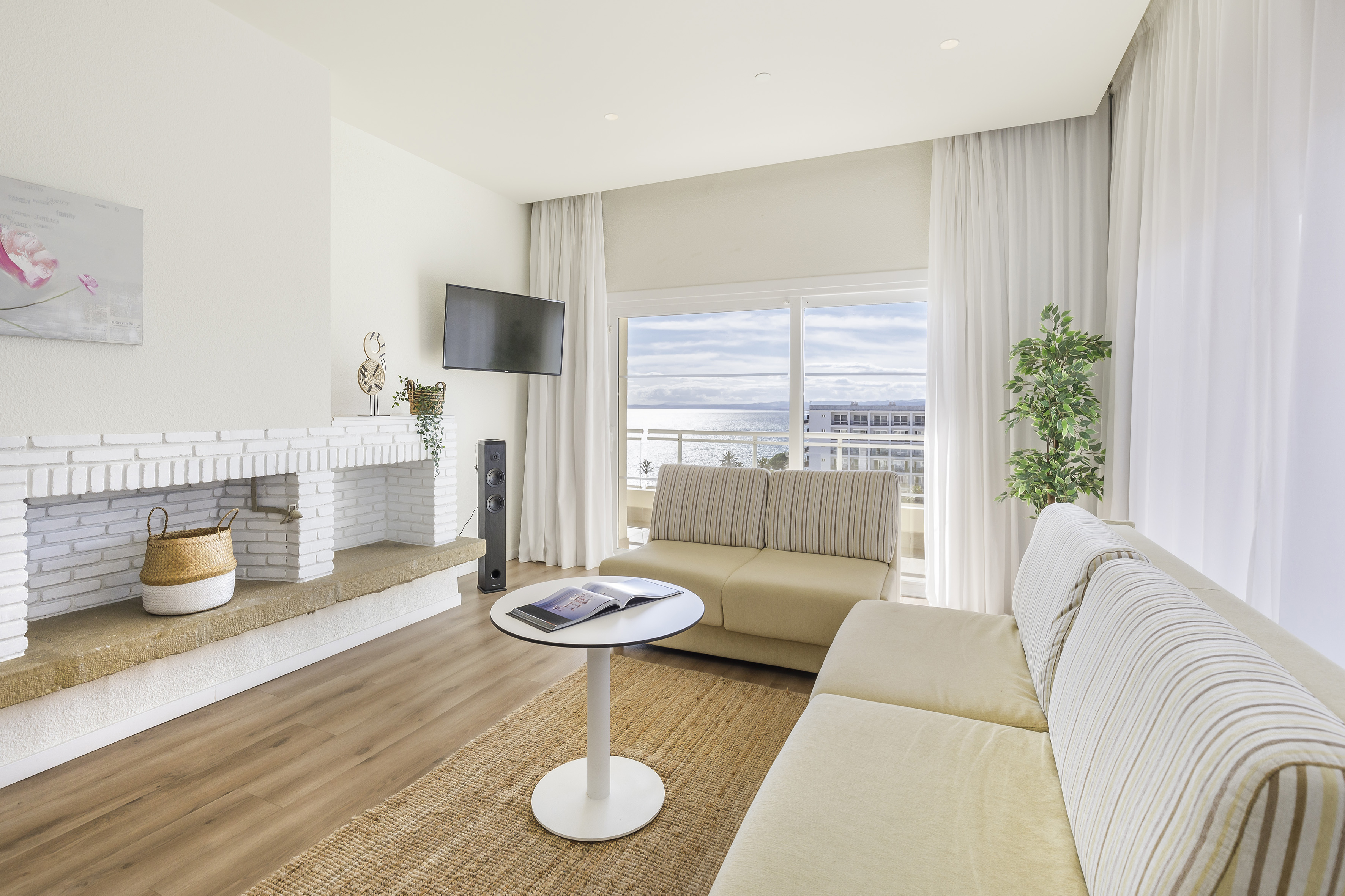 Modern living room with ocean view, beige sofas, and white fireplace.