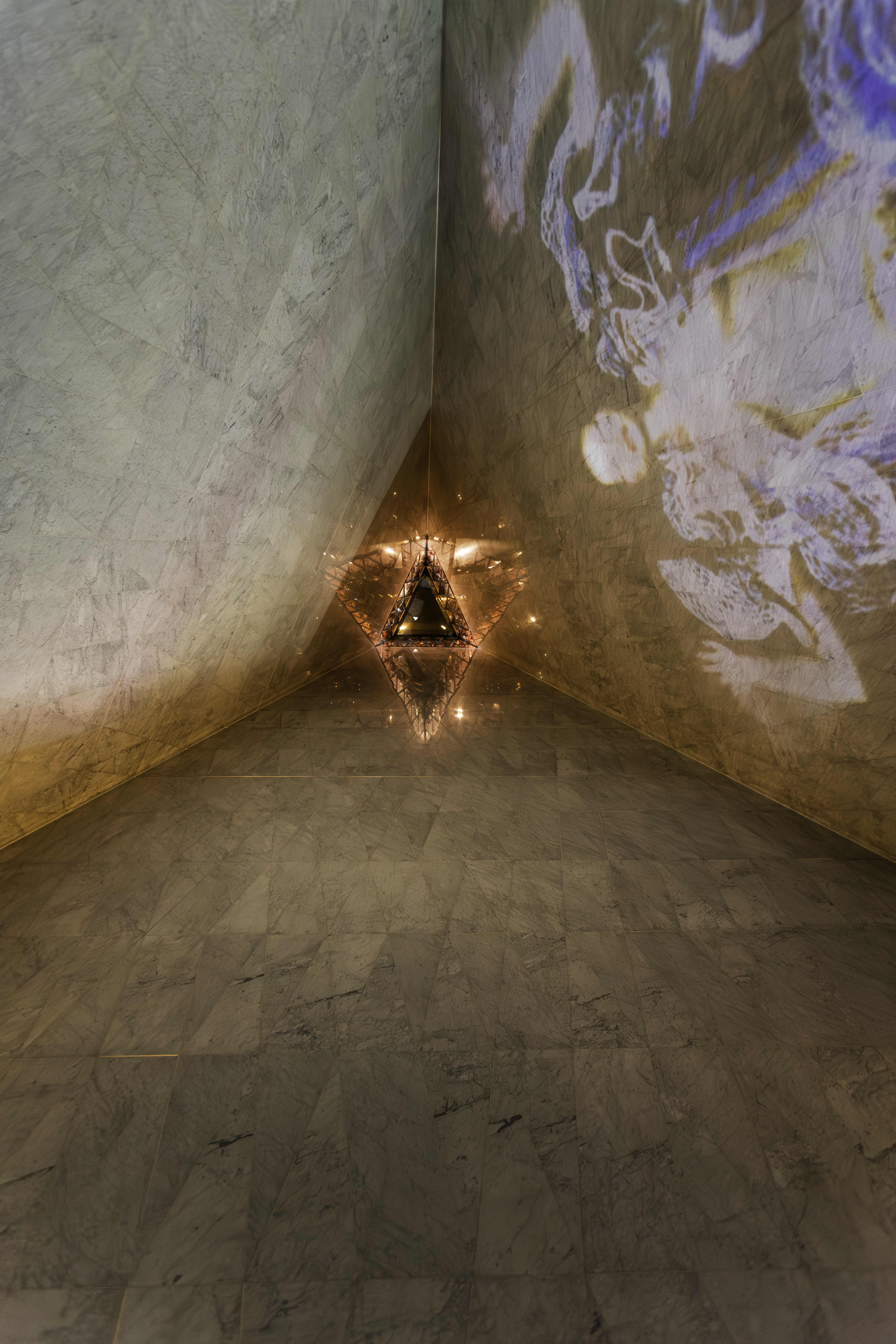 Glowing triangular light in marble corner with abstract projected art.