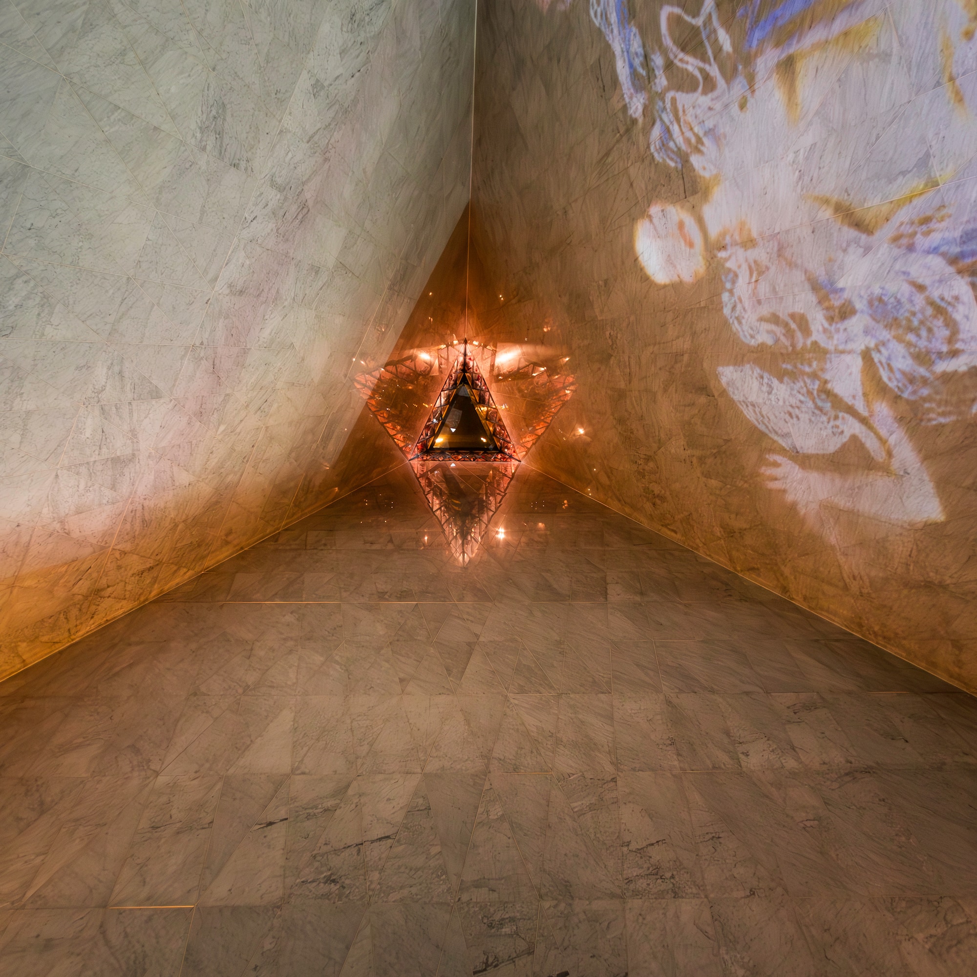 Modern marble interior with glowing triangular light and projected art on wall.