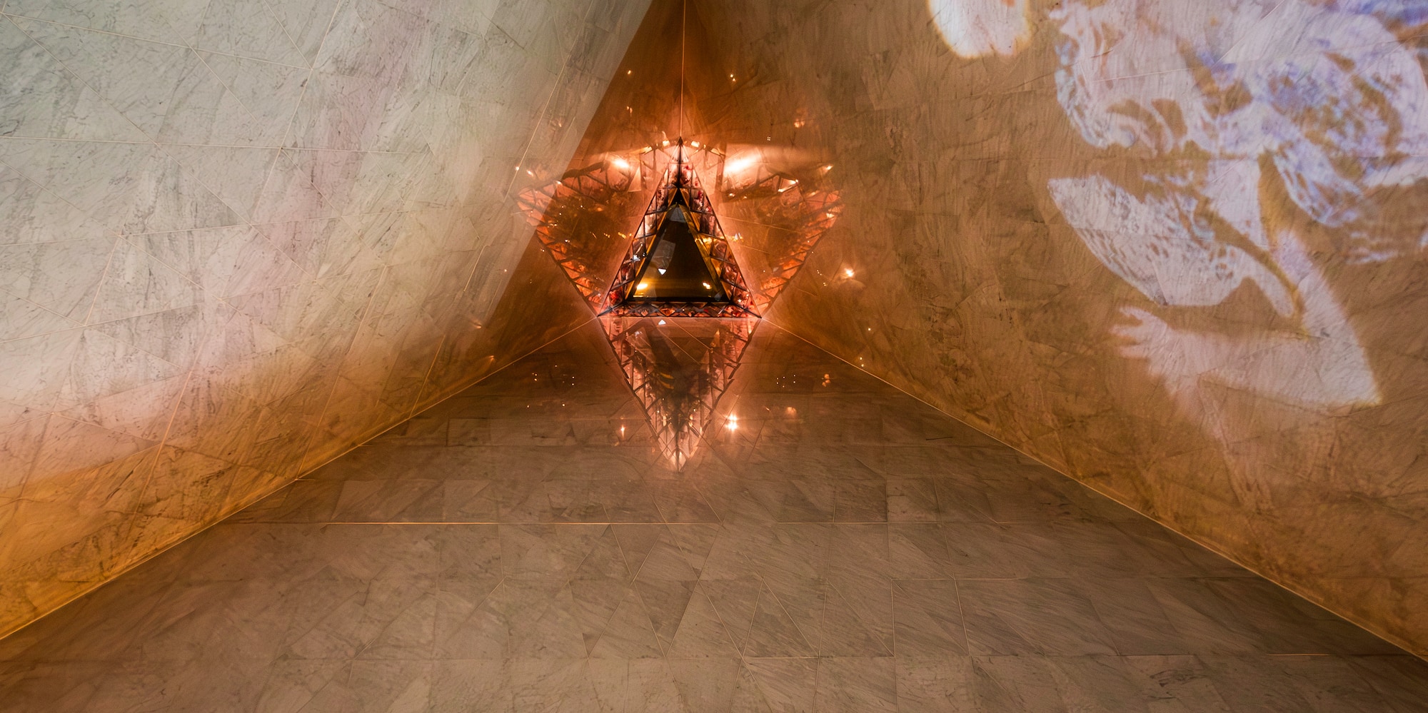 Marble corner with glowing triangular light and projected figure art.