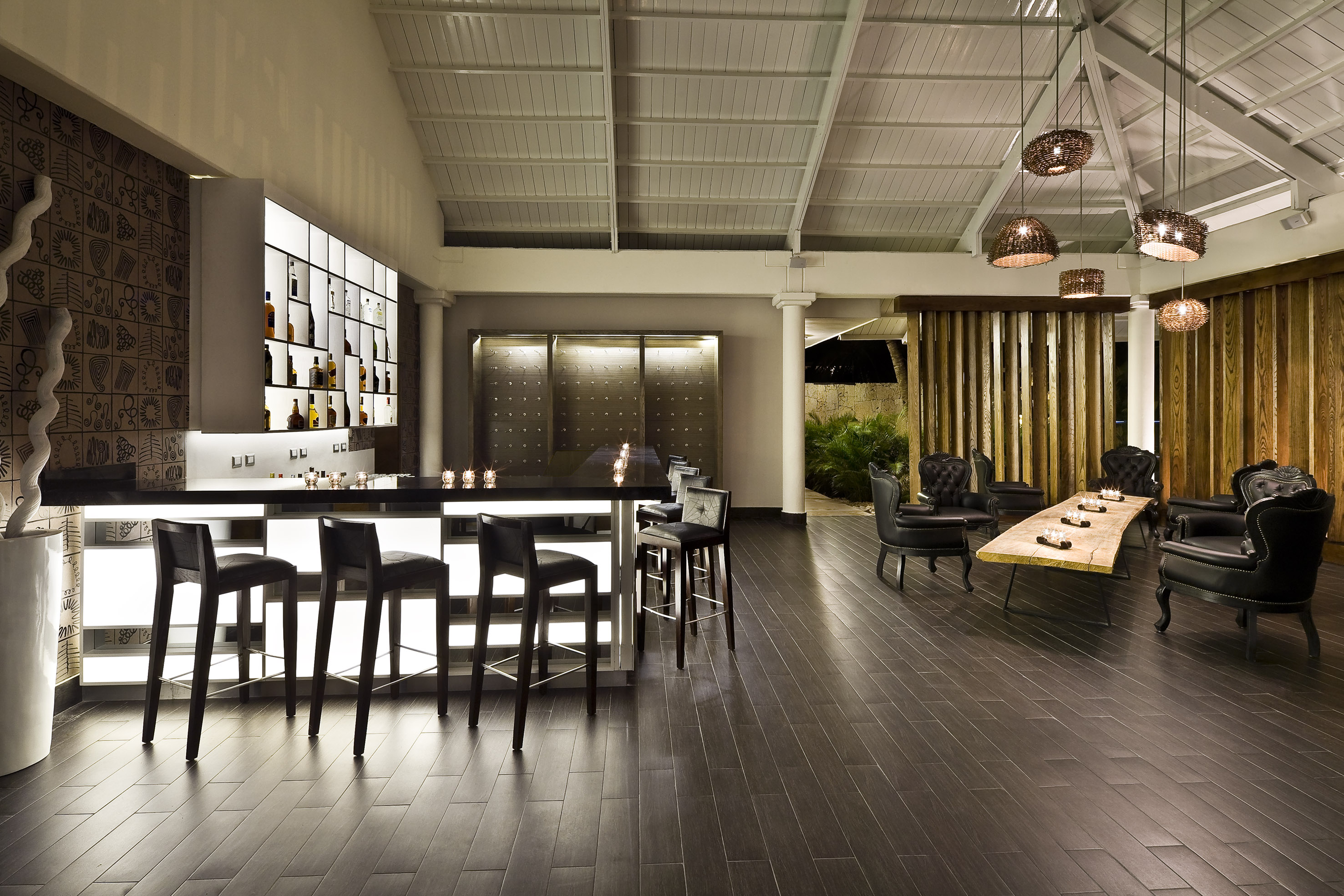 Luxury bar and lounge with backlit bottles, dark wood floor, and leather chairs.