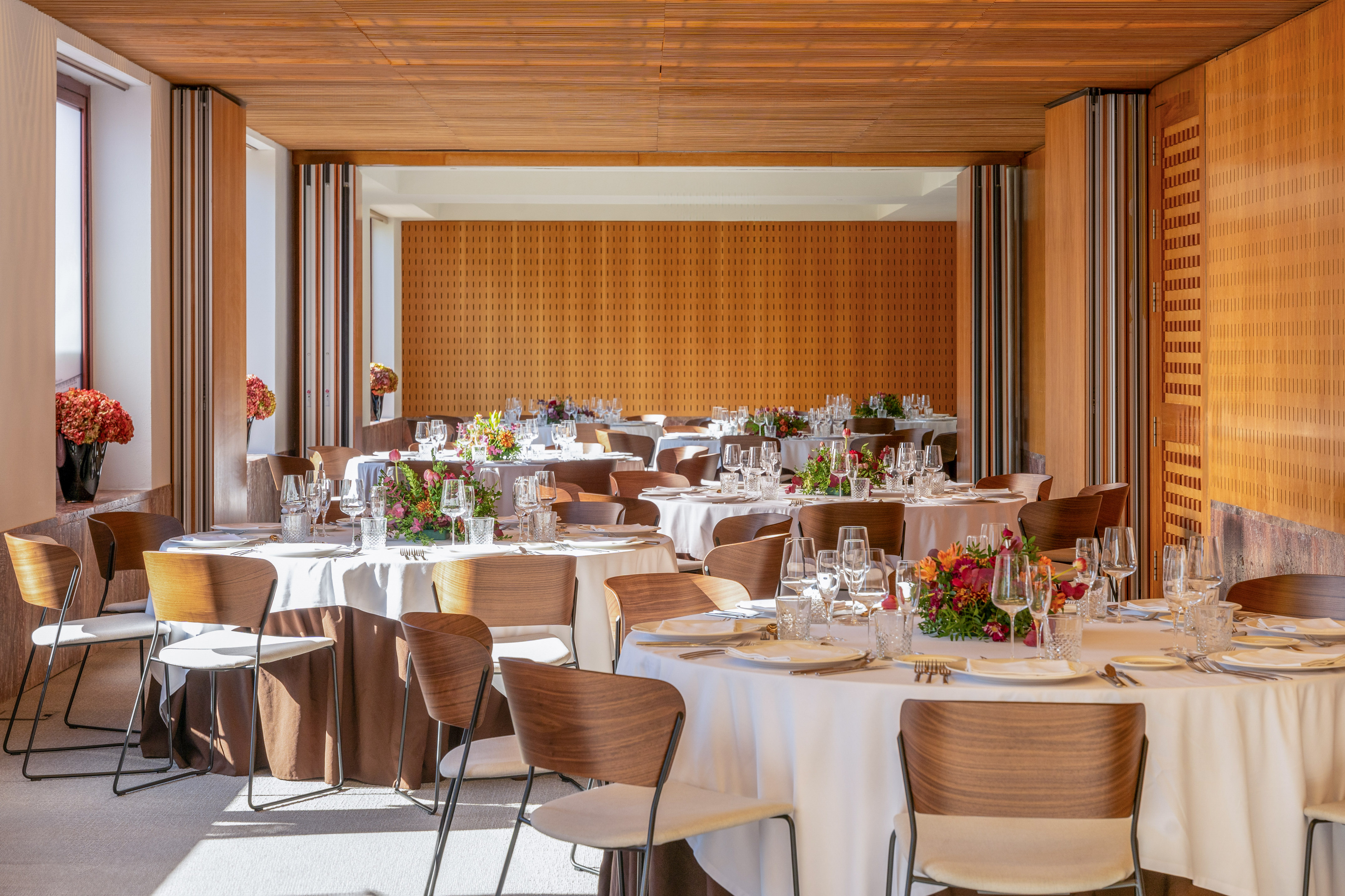 Modern banquet hall with set round tables, floral centerpieces, and wood interior.