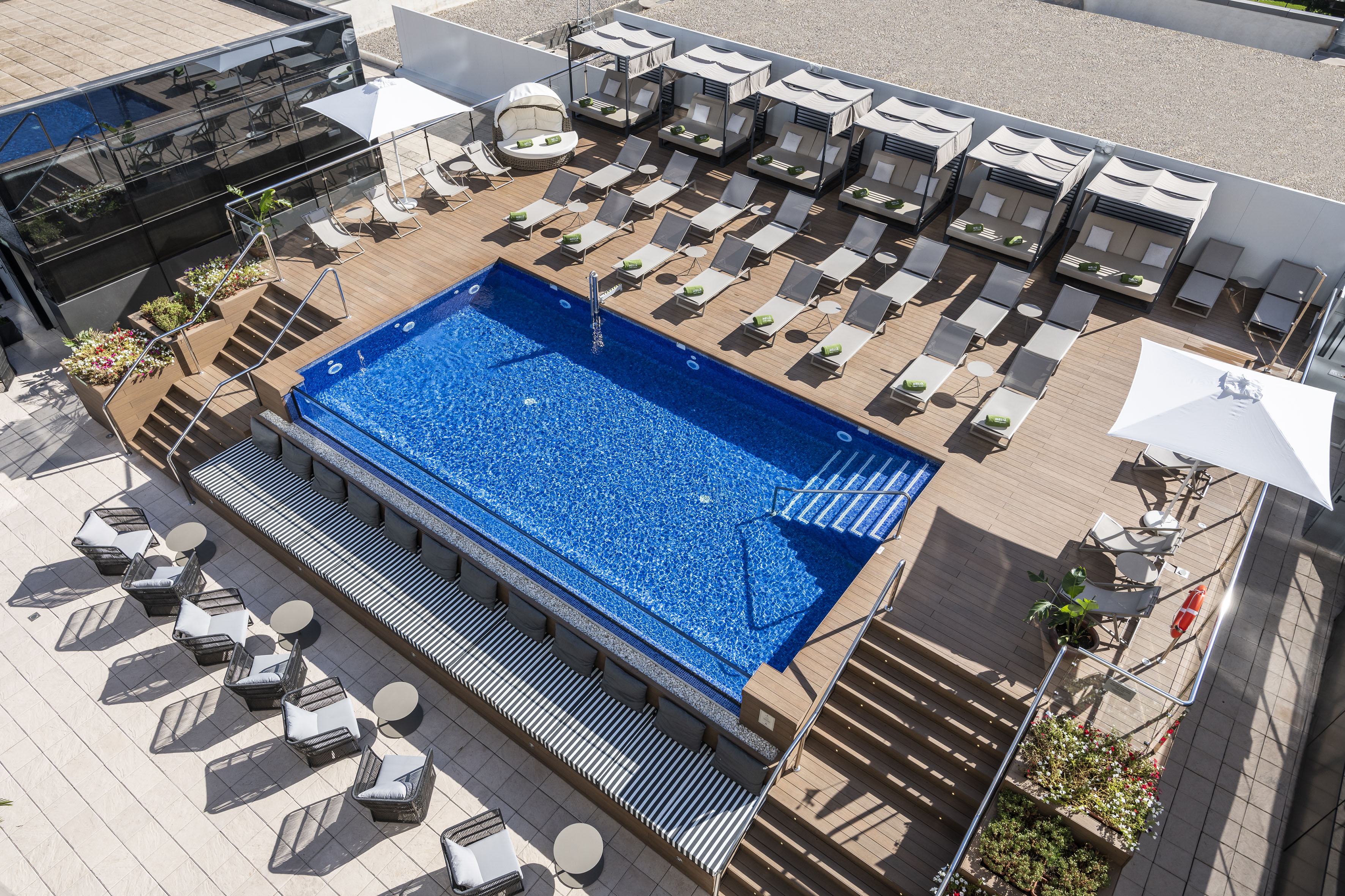 Rooftop hotel pool deck with blue water, sun loungers, and canopy beds.