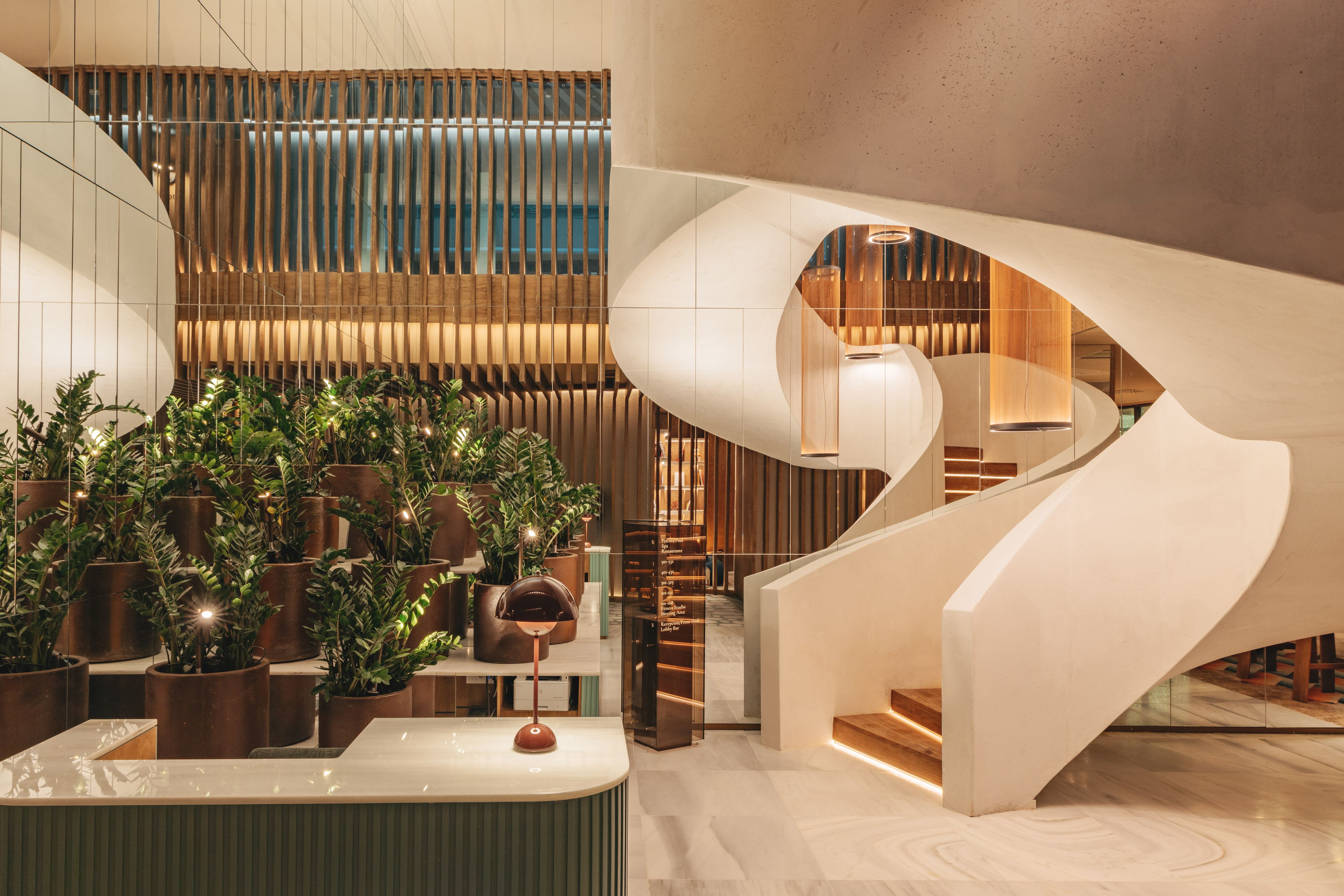 Modern hotel lobby with sculptural staircase, reception desk, and lush greenery.