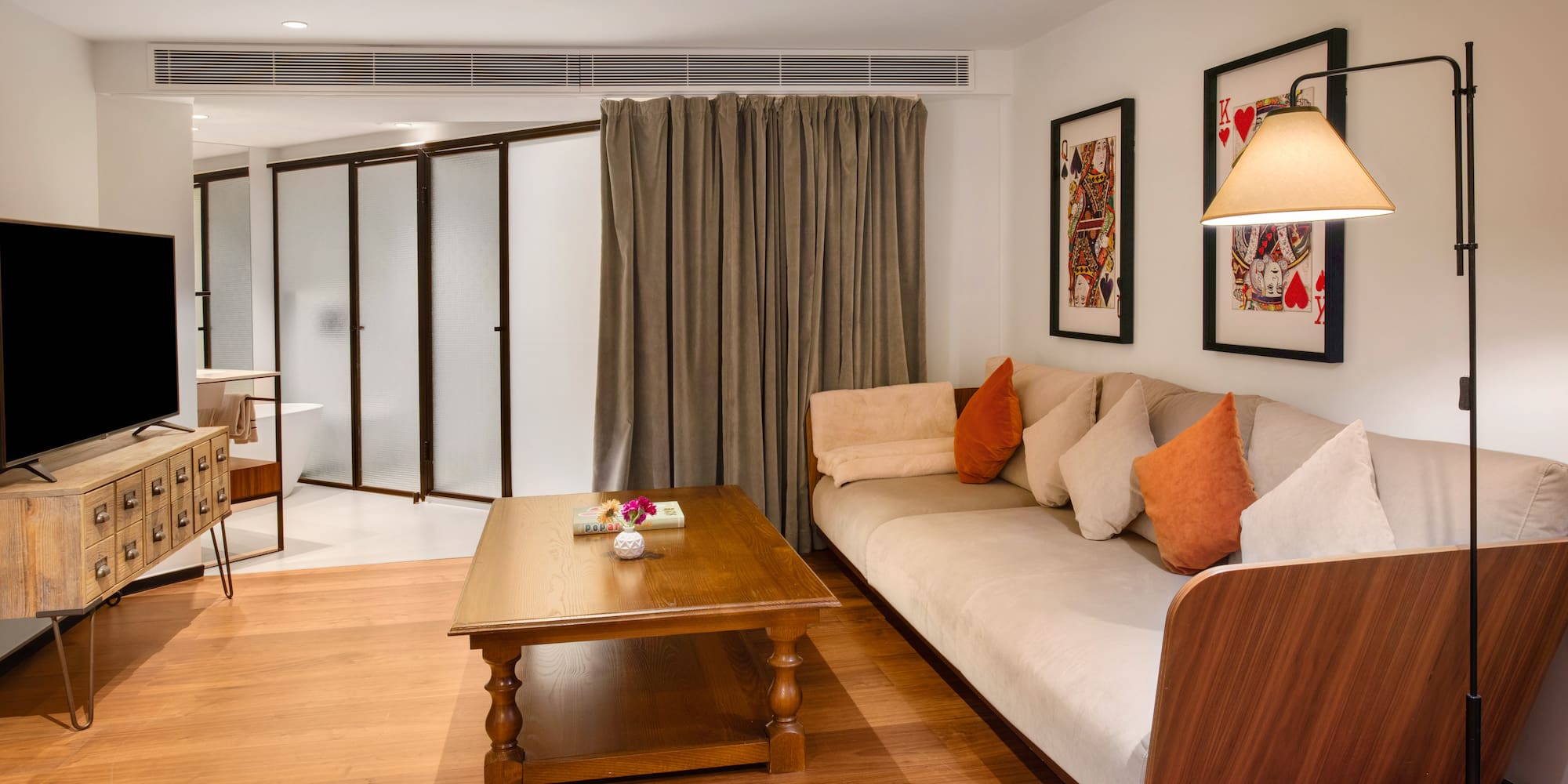 Modern hotel living room with sofa, wooden table, TV, and playing card art.