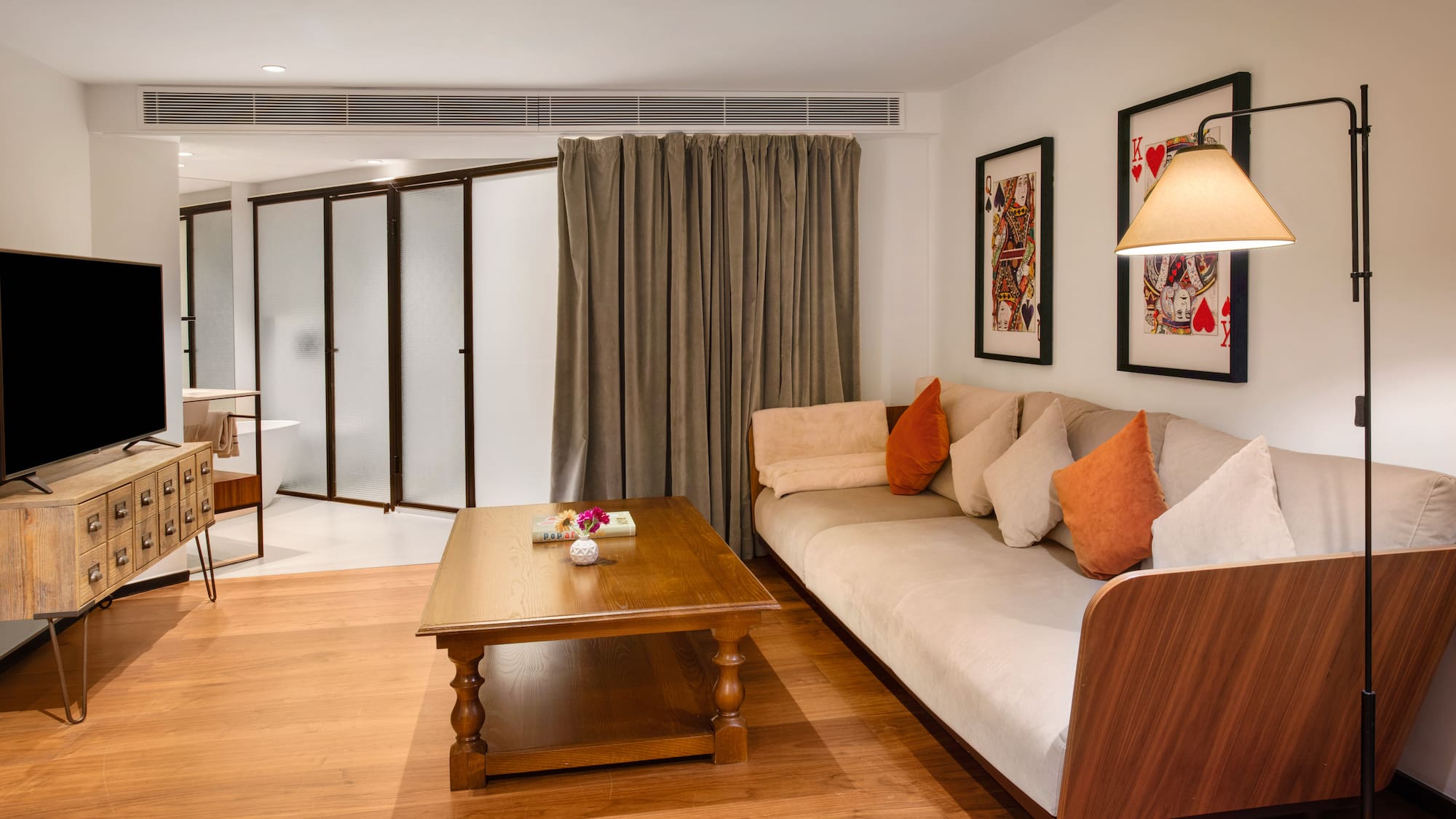 Modern hotel living room with sofa, wooden table, TV, and playing card art.
