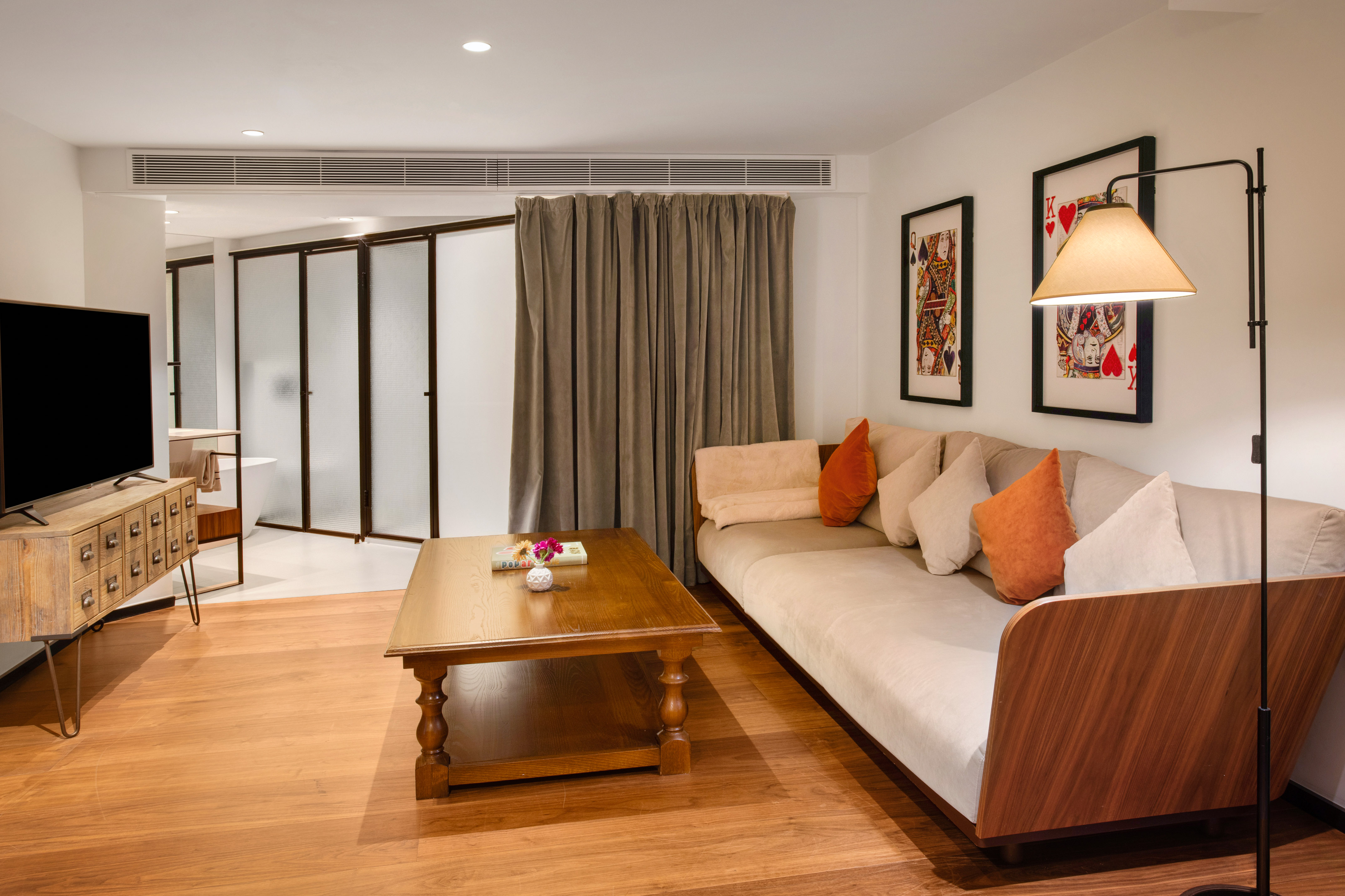 Modern hotel living room with sofa, wooden table, TV, and playing card art.