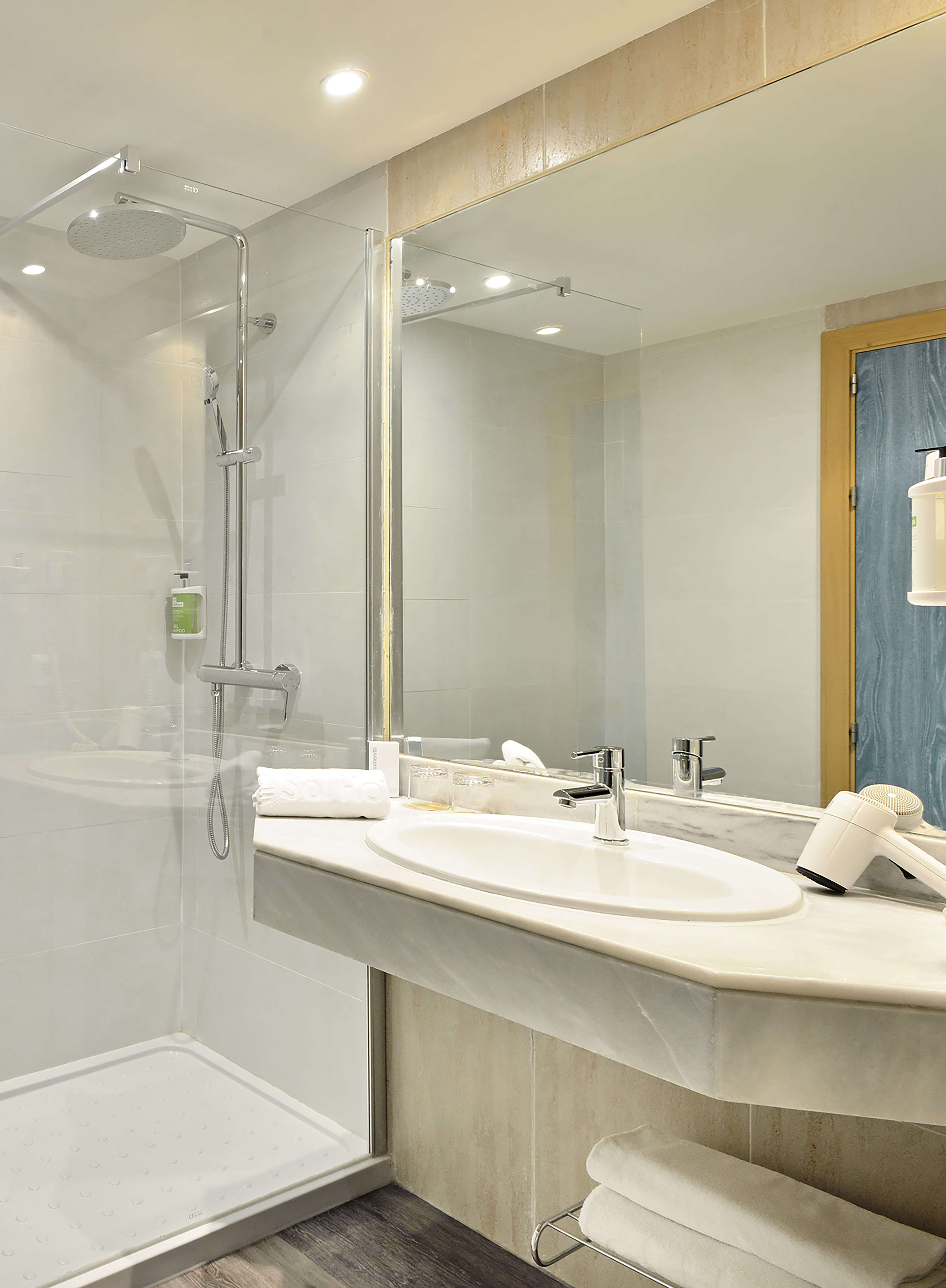 Modern hotel bathroom with glass shower, vanity, mirror, and hairdryer.