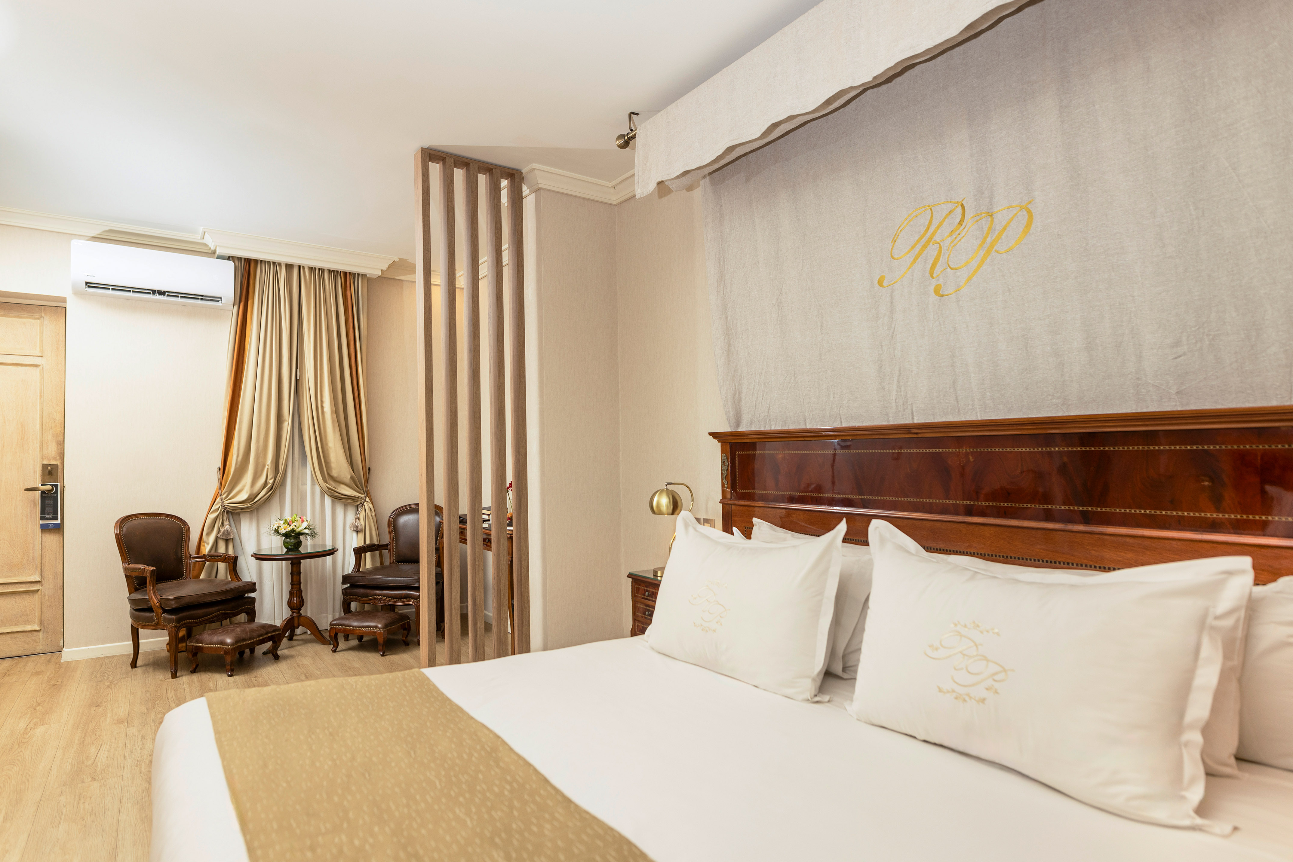 Elegant hotel bedroom with large bed, dark wood, and classic seating.