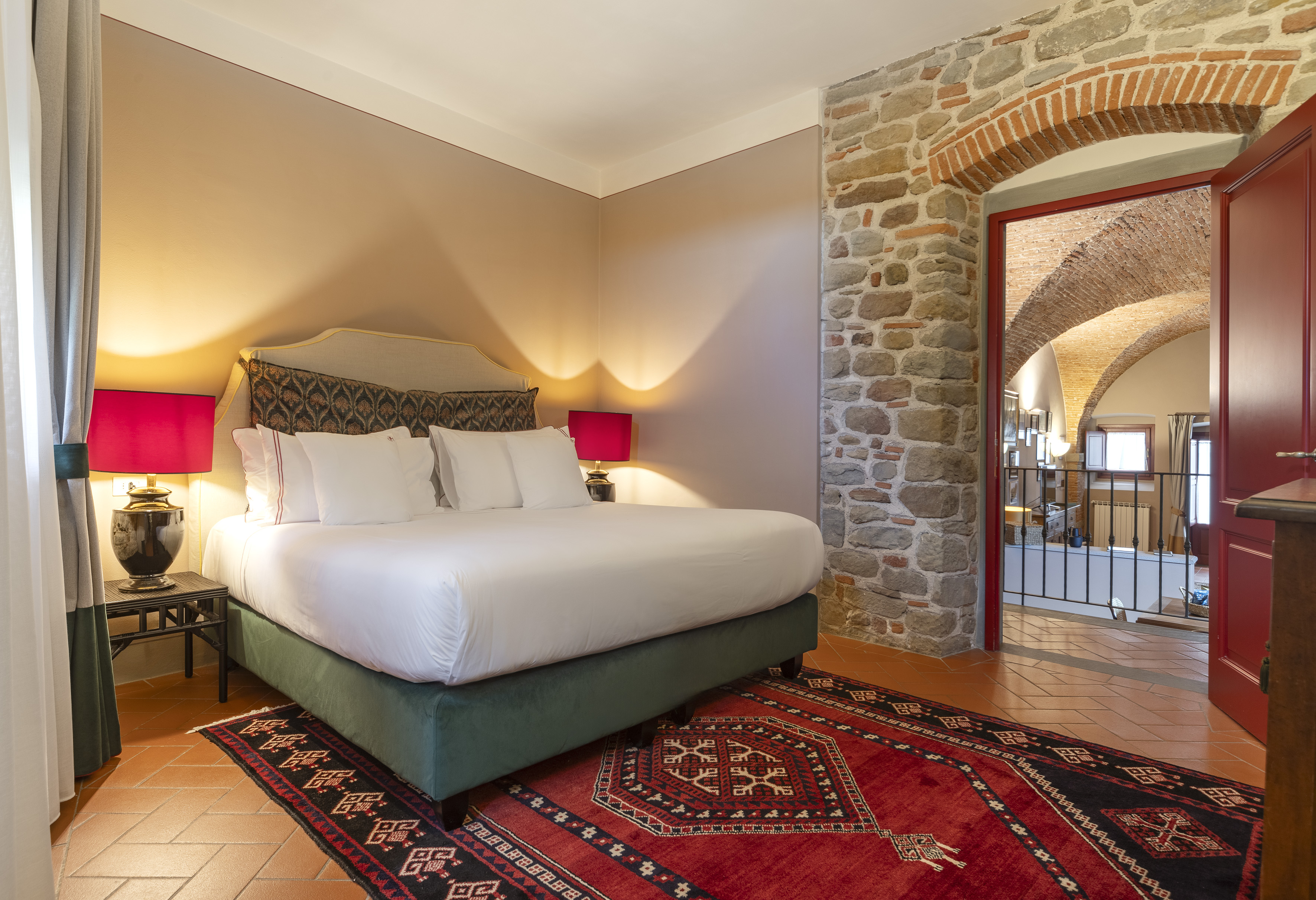 Tuscan style bedroom with king bed, red rug, stone wall, and archway.