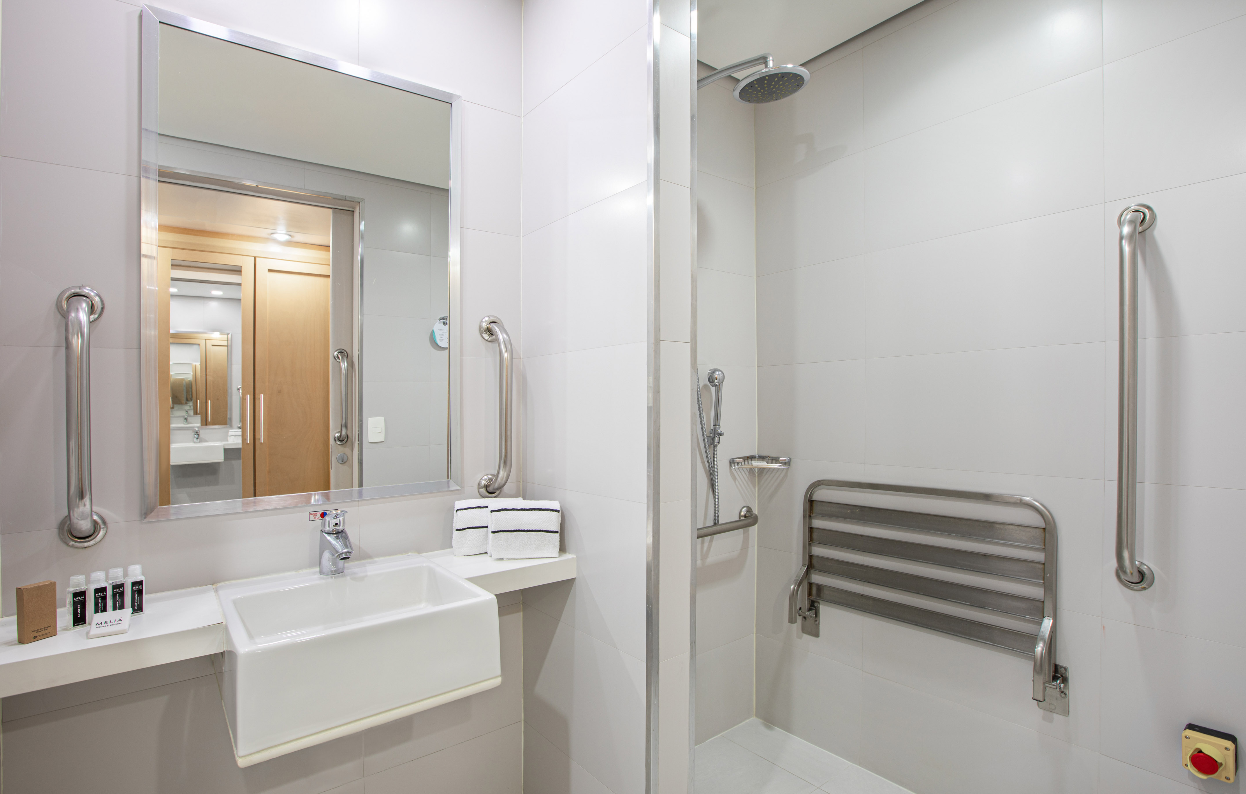 Accessible bathroom with white tiles, grab bars, shower, and fold-down seat.
