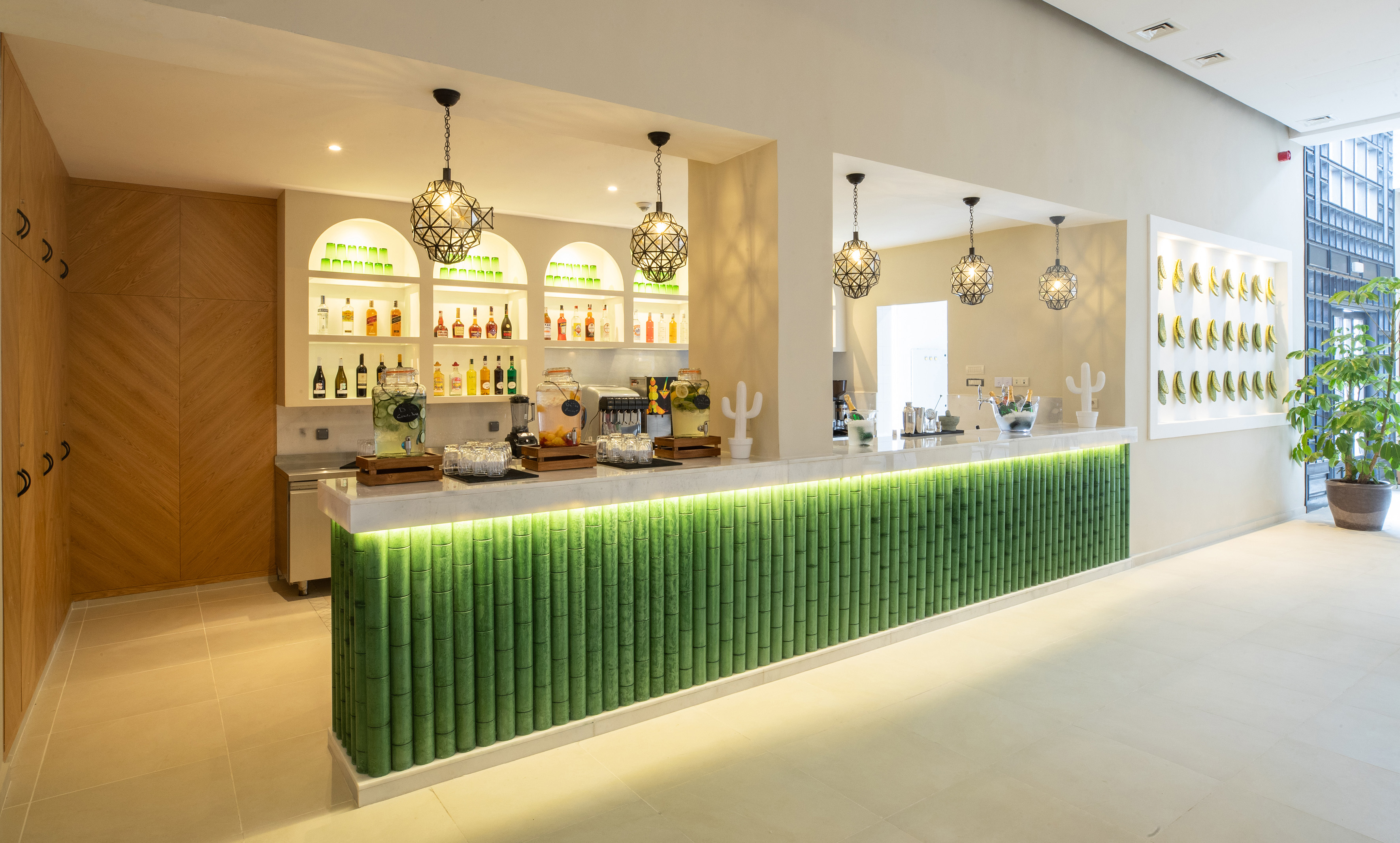 Modern hotel bar with illuminated green bamboo counter and juice dispensers.