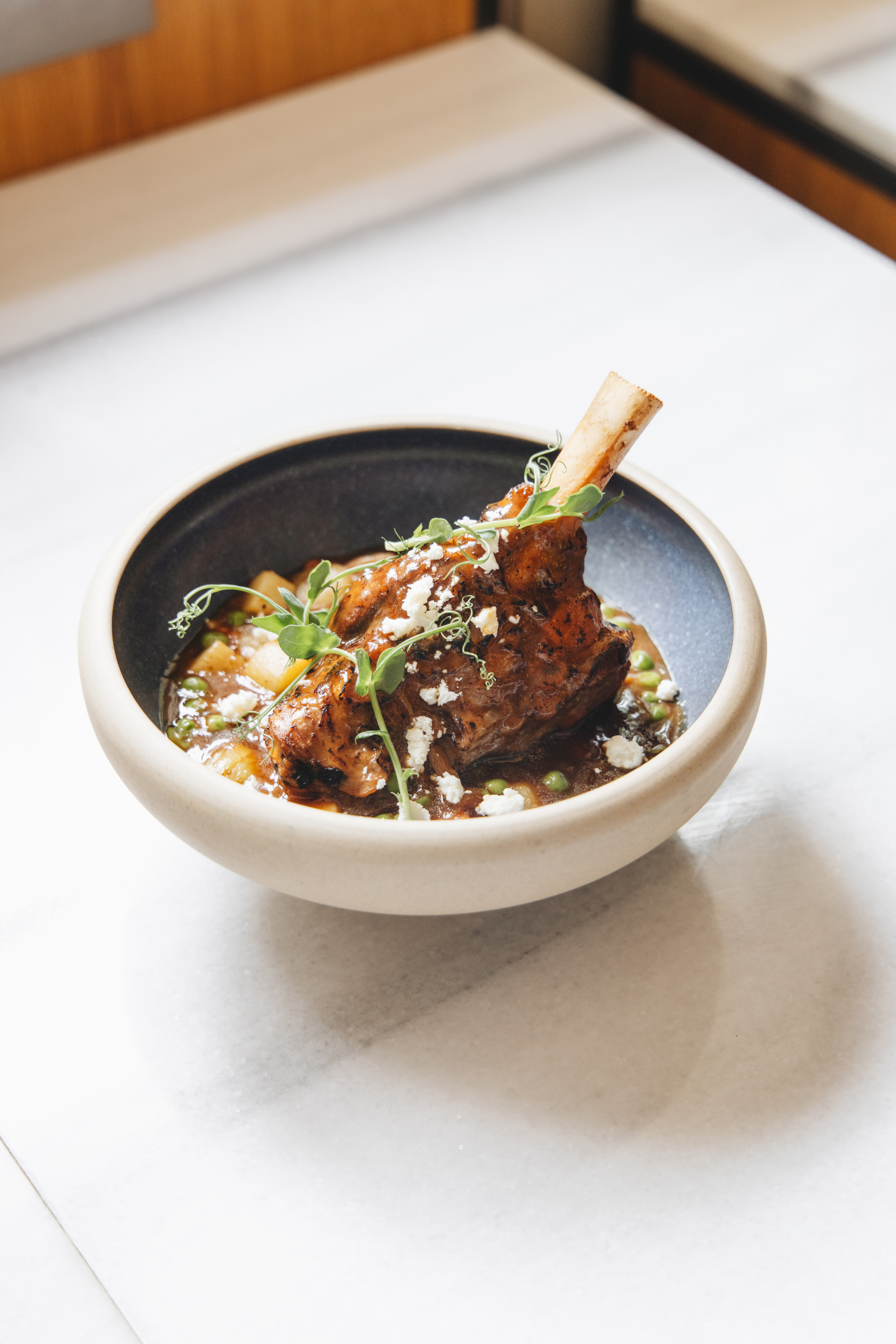 Braised lamb shank with peas, potatoes, feta, and microgreens.