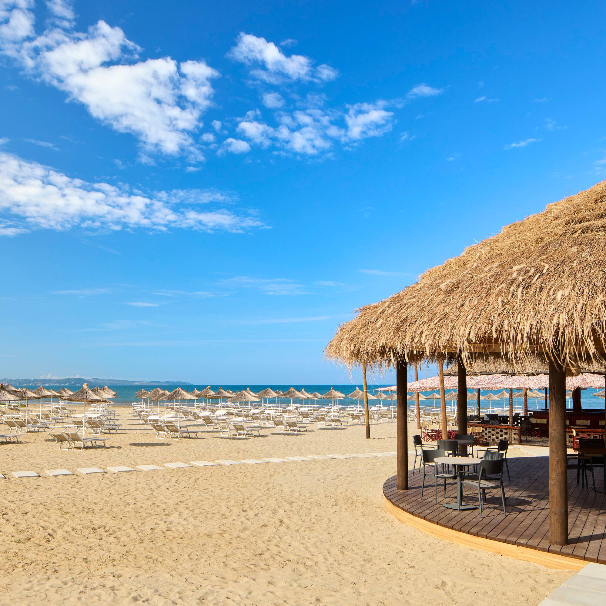 a beach with a thatched roof and chairs