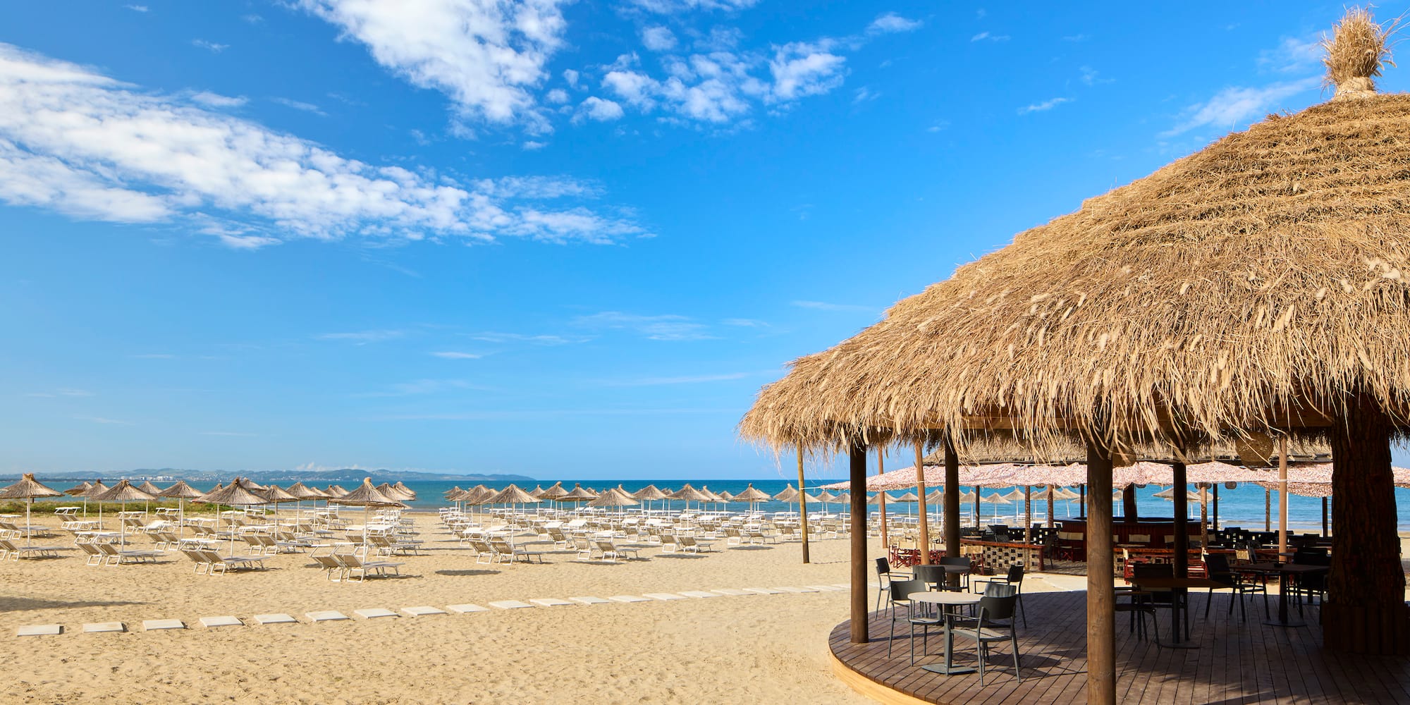 a beach with a thatched roof and chairs