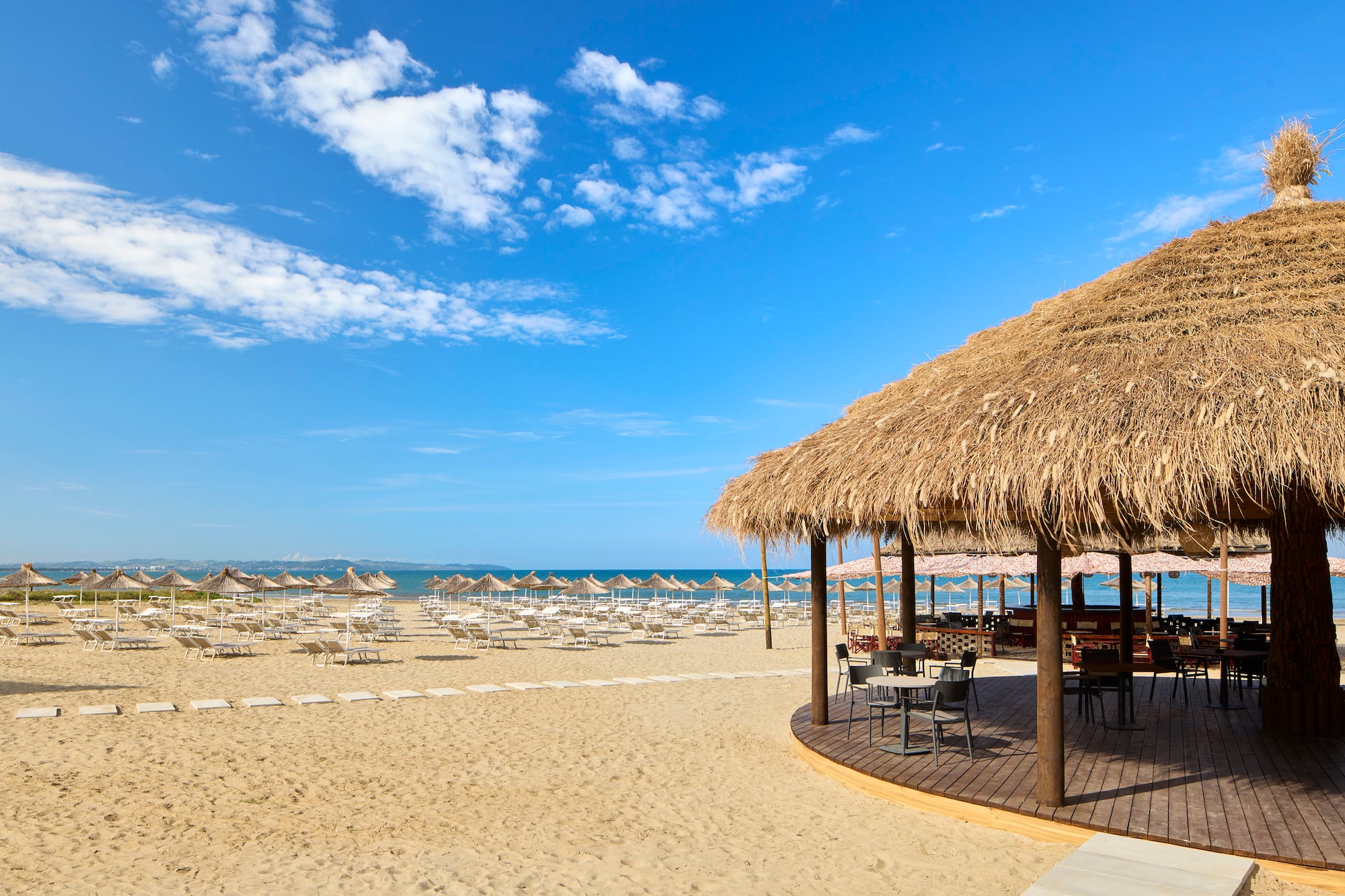 a beach with a thatched roof and chairs