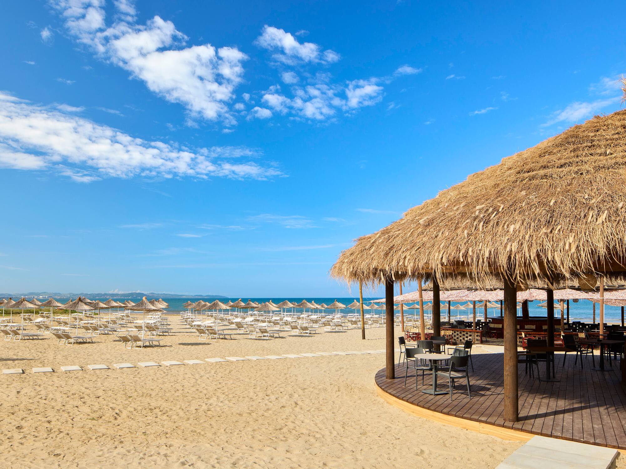 a beach with a thatched roof and chairs